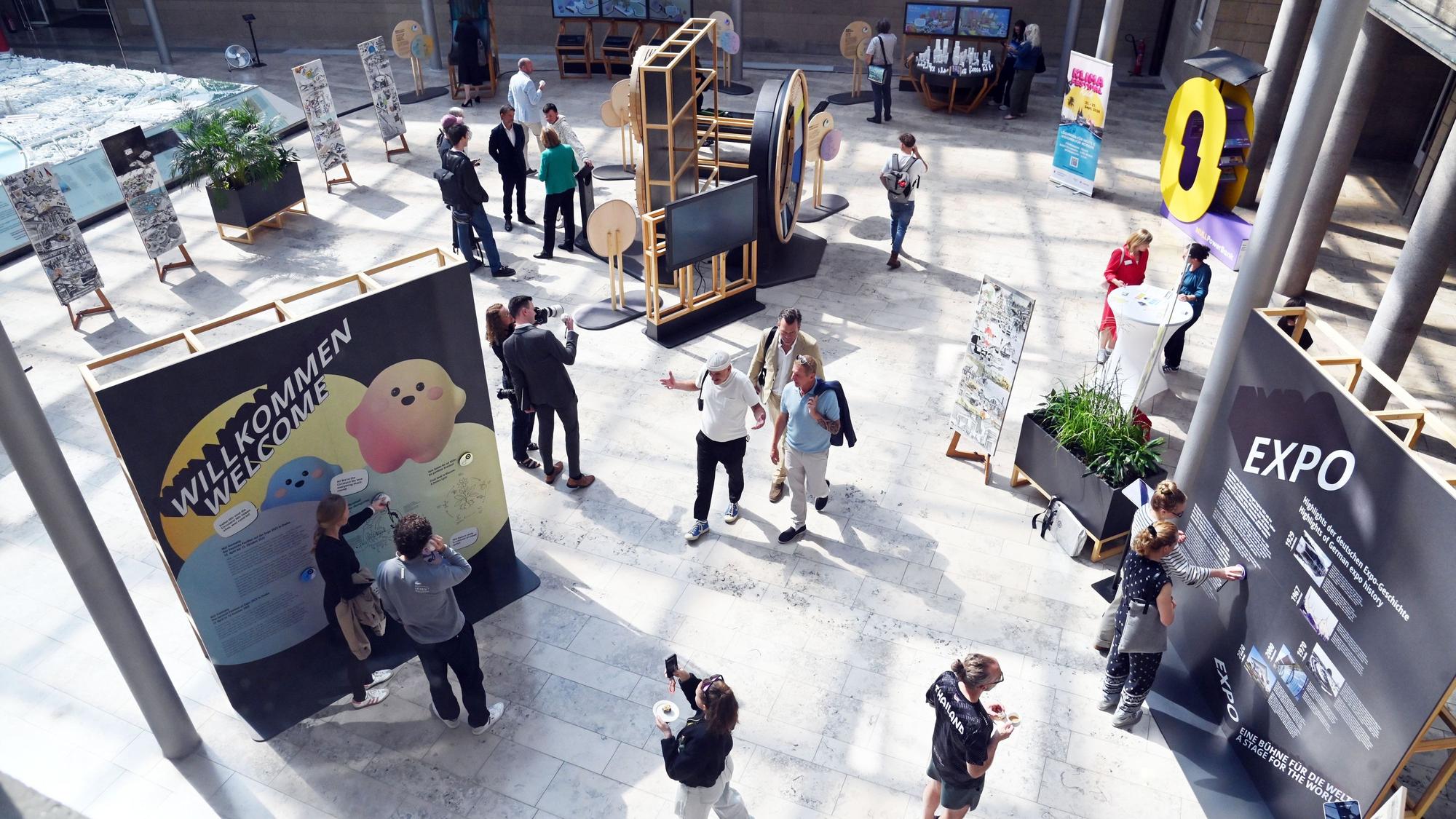 Die Ausstellung ist von oben zu sehen, Menschen stehen an den einzelnen Exponaten.