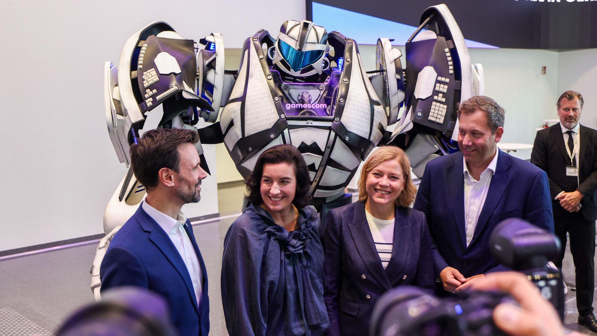 Felix Falk, Dorothee Bär, Henna Virkkunen und Lars Klingbeil stehen zur Eröffnung der Messe Gamescom vor einem Transformer-Roboter.