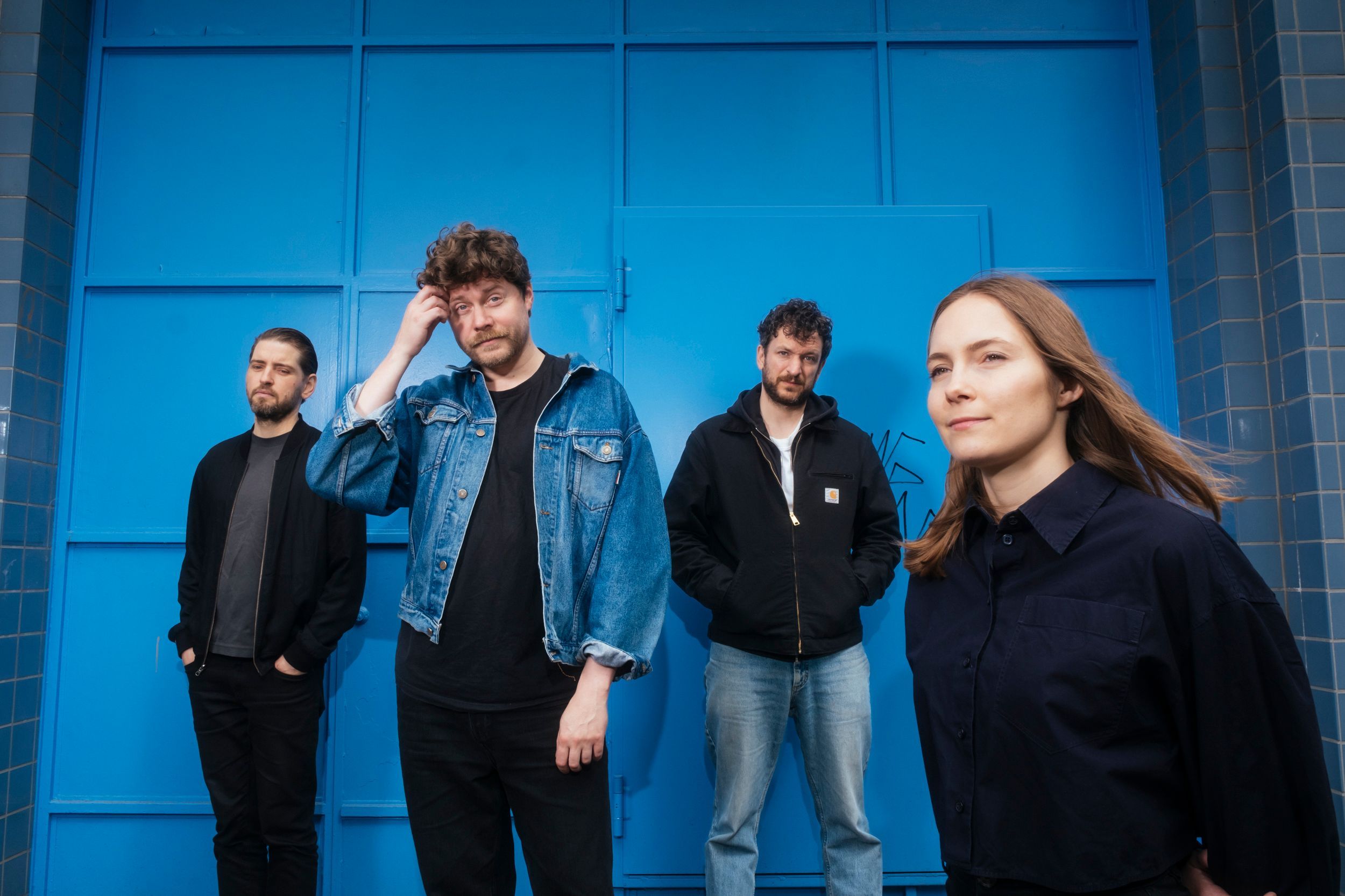 Vier Menschen stehen nebeneinander vor einer blauen Wand.