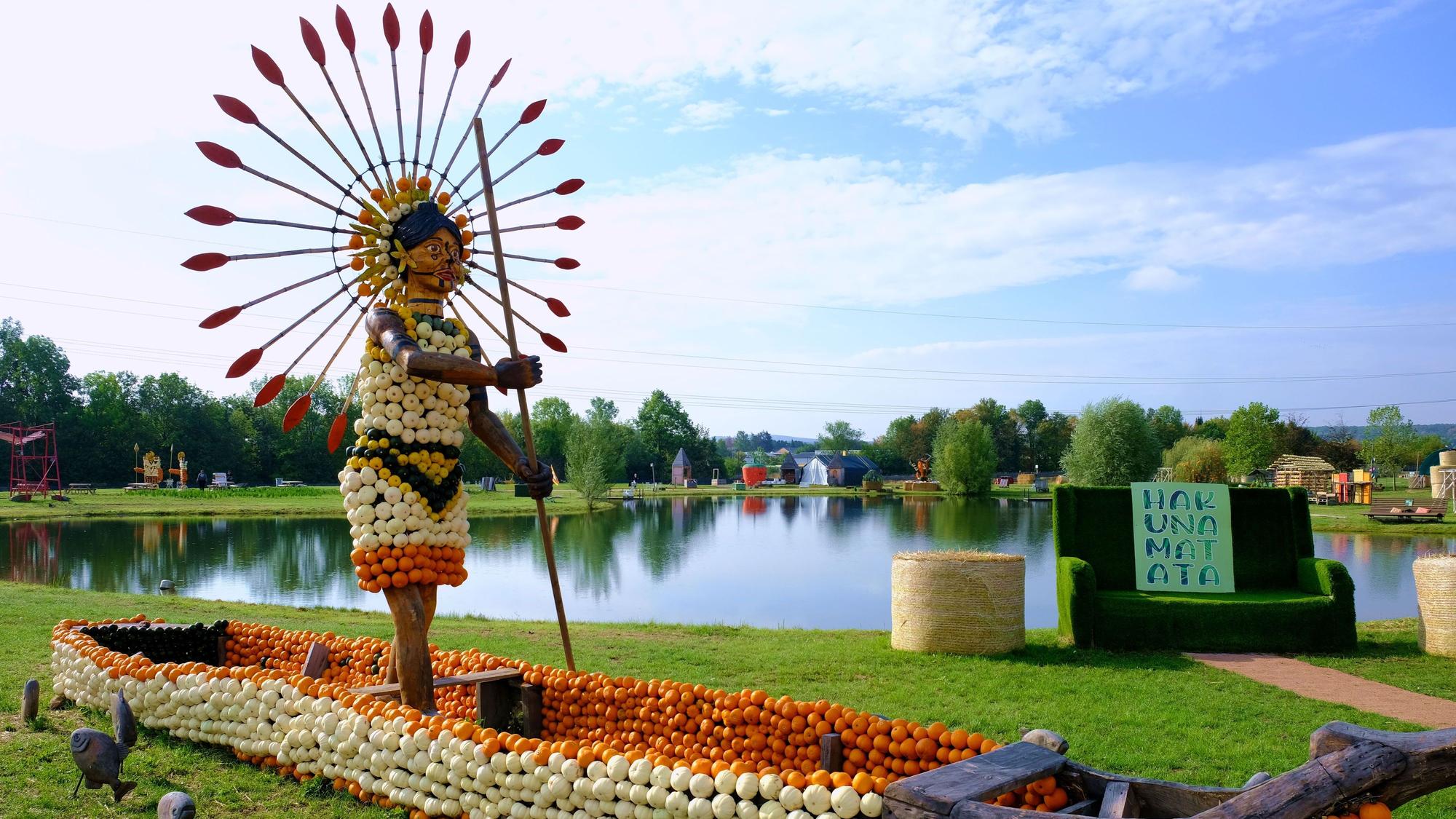 In einem Kürbis-Kanu steht die aus Kürbissen gestaltete Figur einer indigenen Person, die einen strahlenförmigen Kopfschmuck trägt.