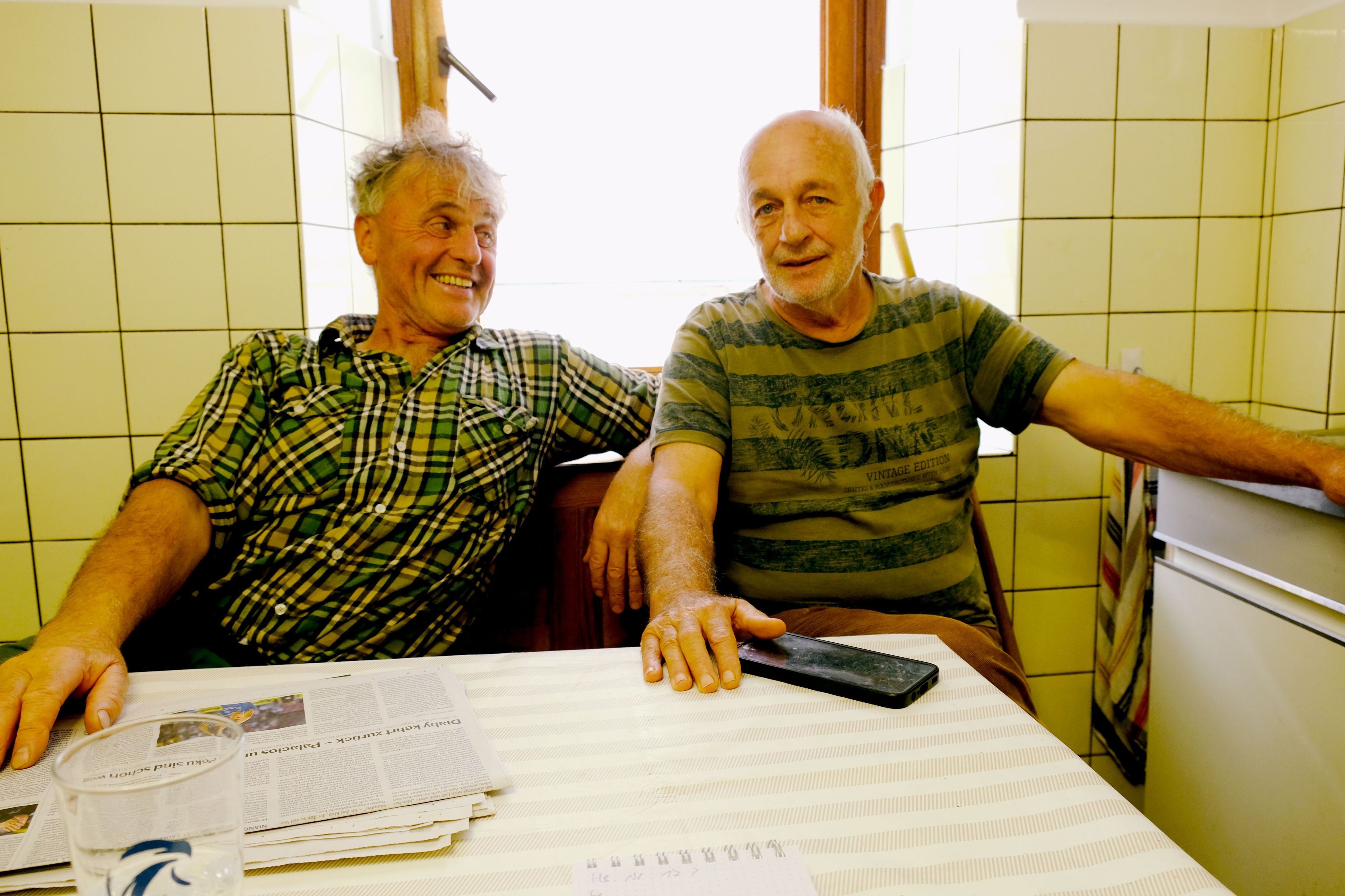 Paul Milz und Werner Müller sitzen vor einer gefliesten Wand mit Fenster am Küchentisch.