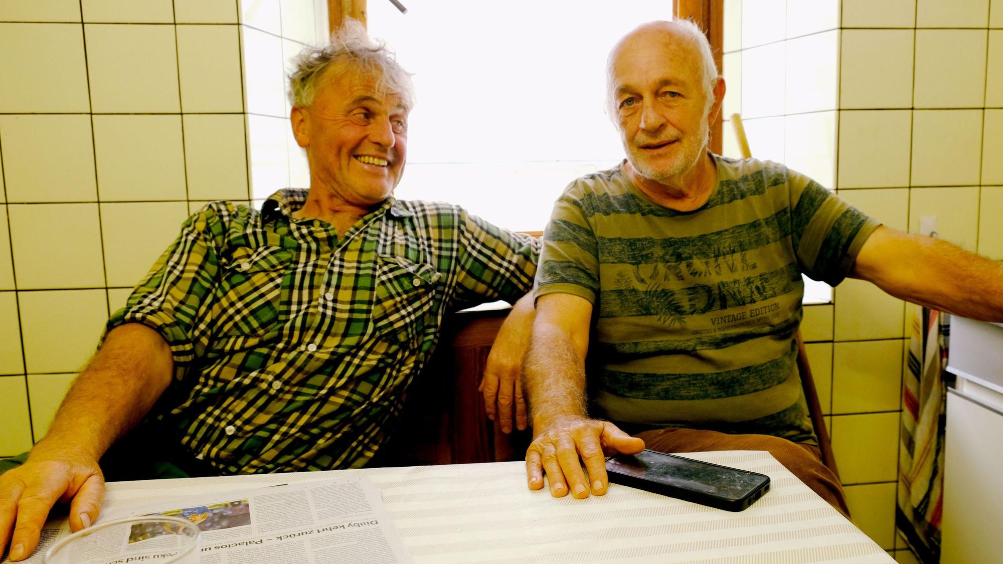Paul Milz und Werner Müller sitzen vor einer gefliesten Wand mit Fenster am Küchentisch.