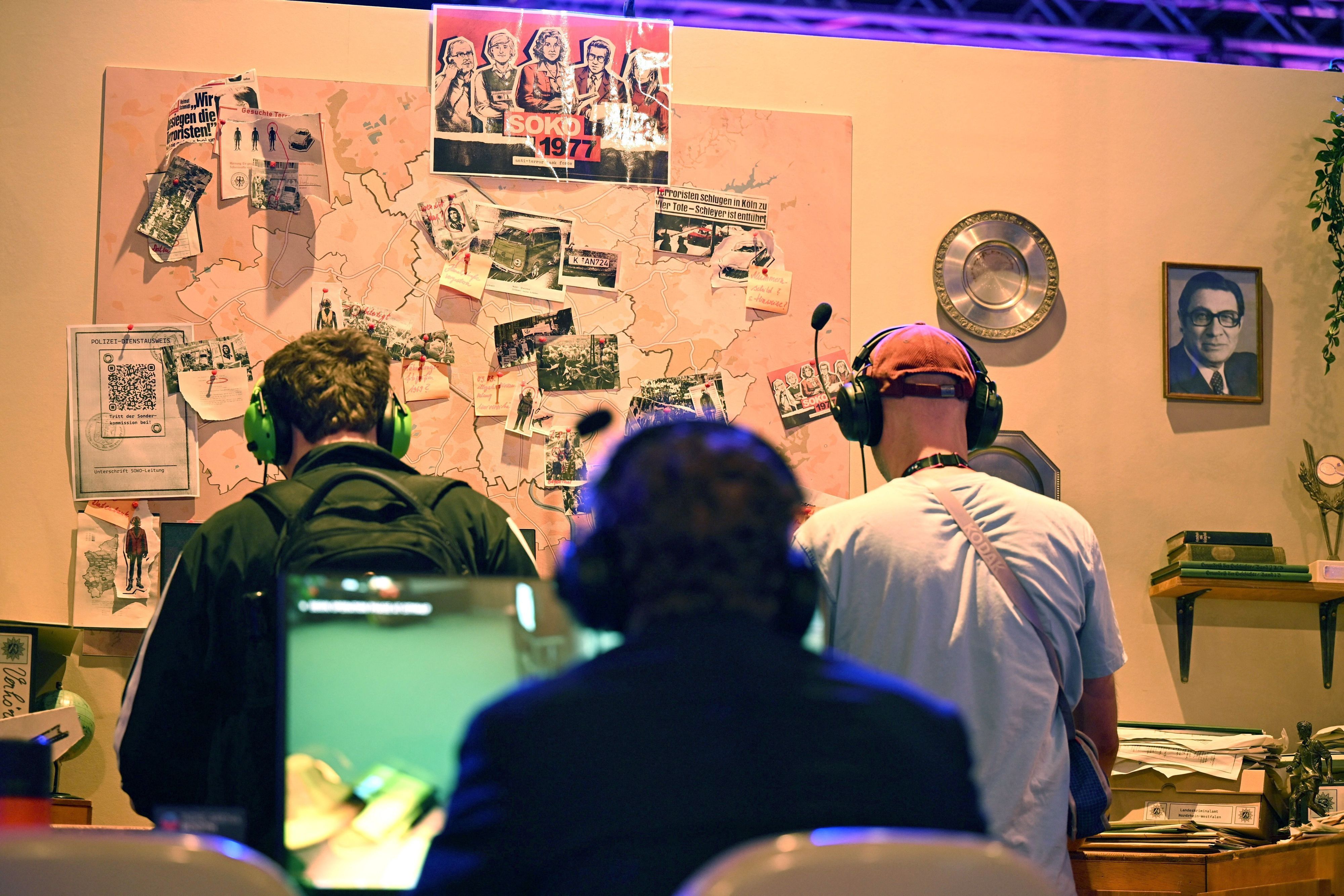 Besucher der Gamescom sitzen am Messestand der Bundeszentrale für politische Bildung und spielen das Serious Game „Soko 1977“, das den RAF-Terror der 1970er Jahre thematisiert und vom Berliner Studio Paintbucket Game entwickelt wurde.