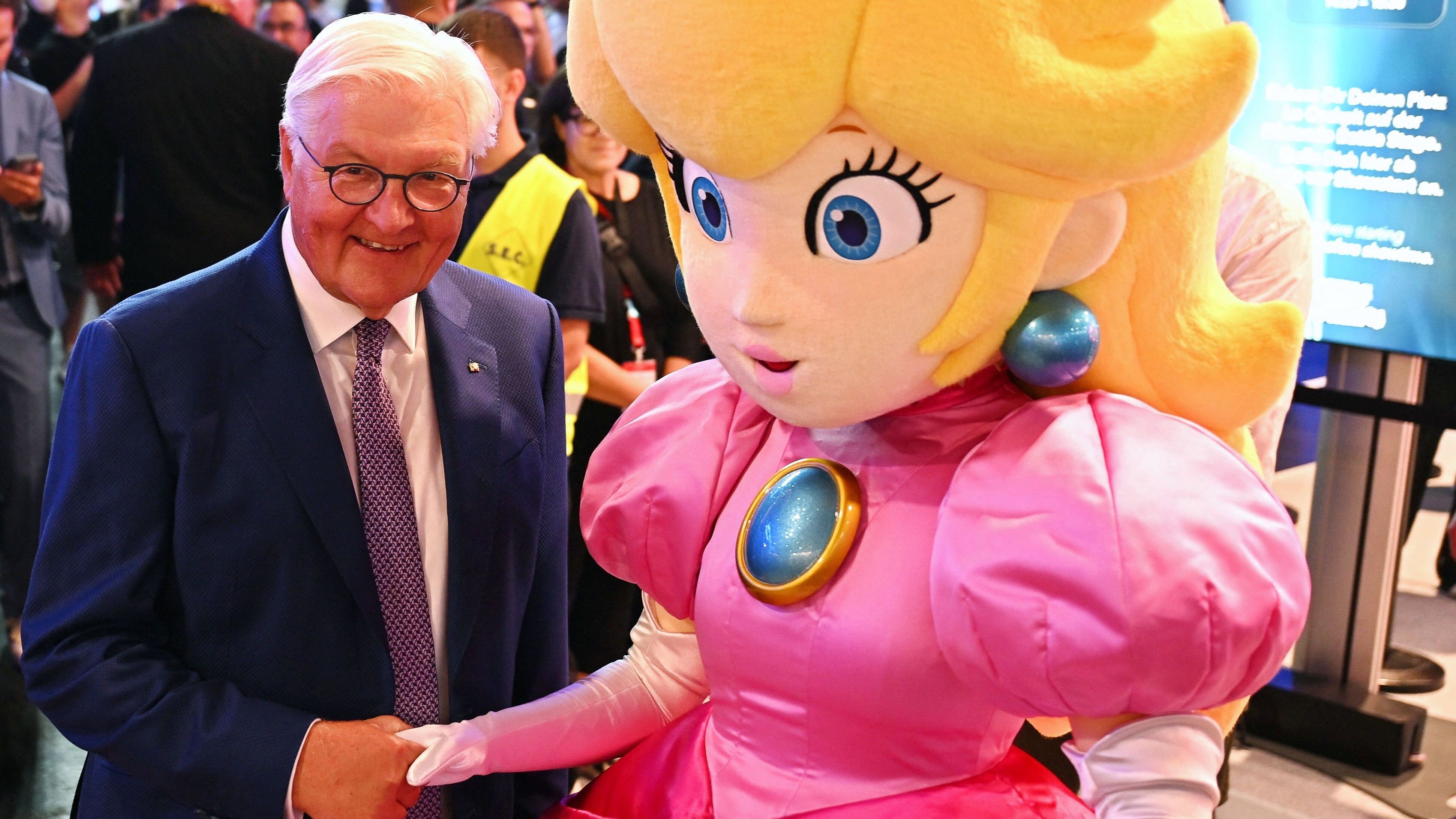 Bundespräsident Frank-Walter Steinmeier wird bei einem Rundgang über die Gamescom am Nintendo-Messestand von Prinzessin Peach begrüßt, einer Figur aus der Super-Mario-Reihe.