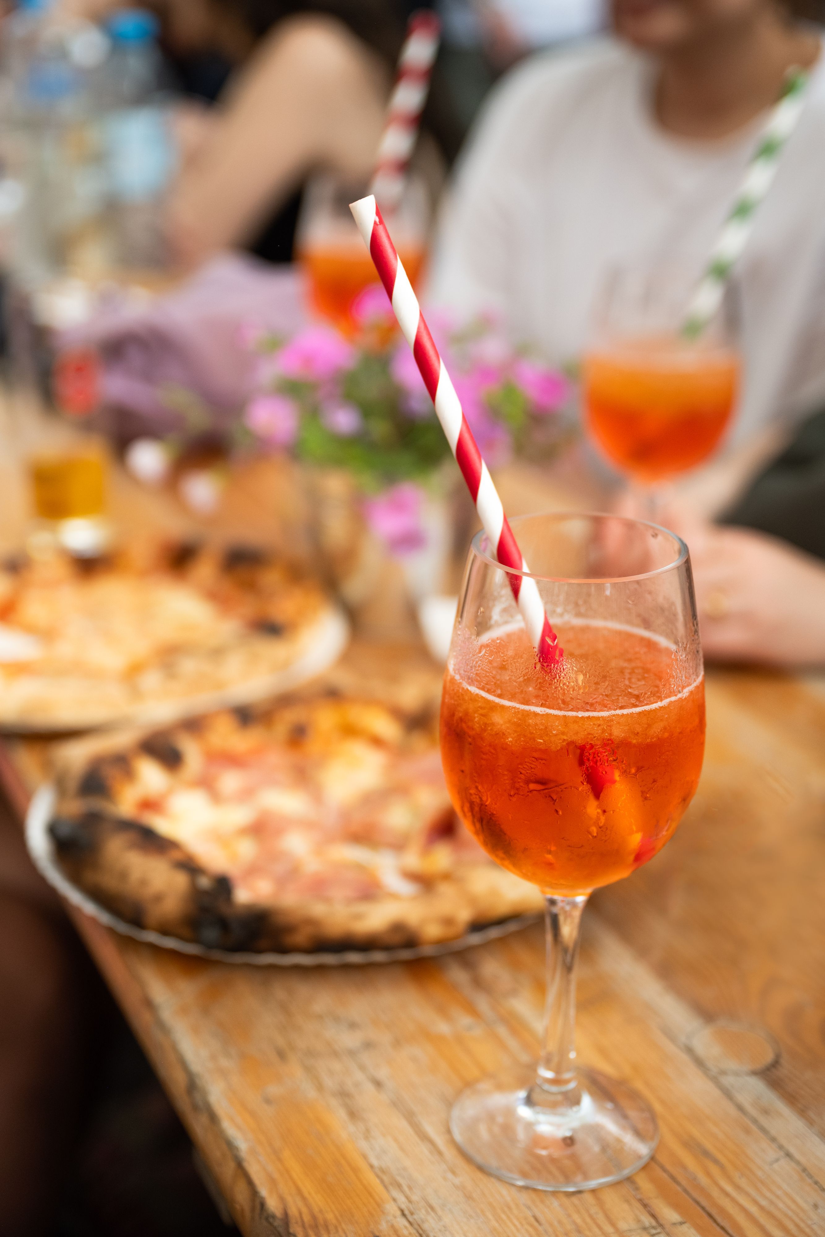 Ein Glas Aperol Spritz steht vor zwei Pizzen auf einem hölzernen Tisch. (Symbolbild)