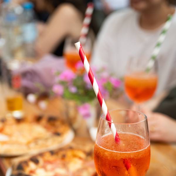 Ein Glas Aperol Spritz steht vor zwei Pizzen auf einem hölzernen Tisch. (Symbolbild)