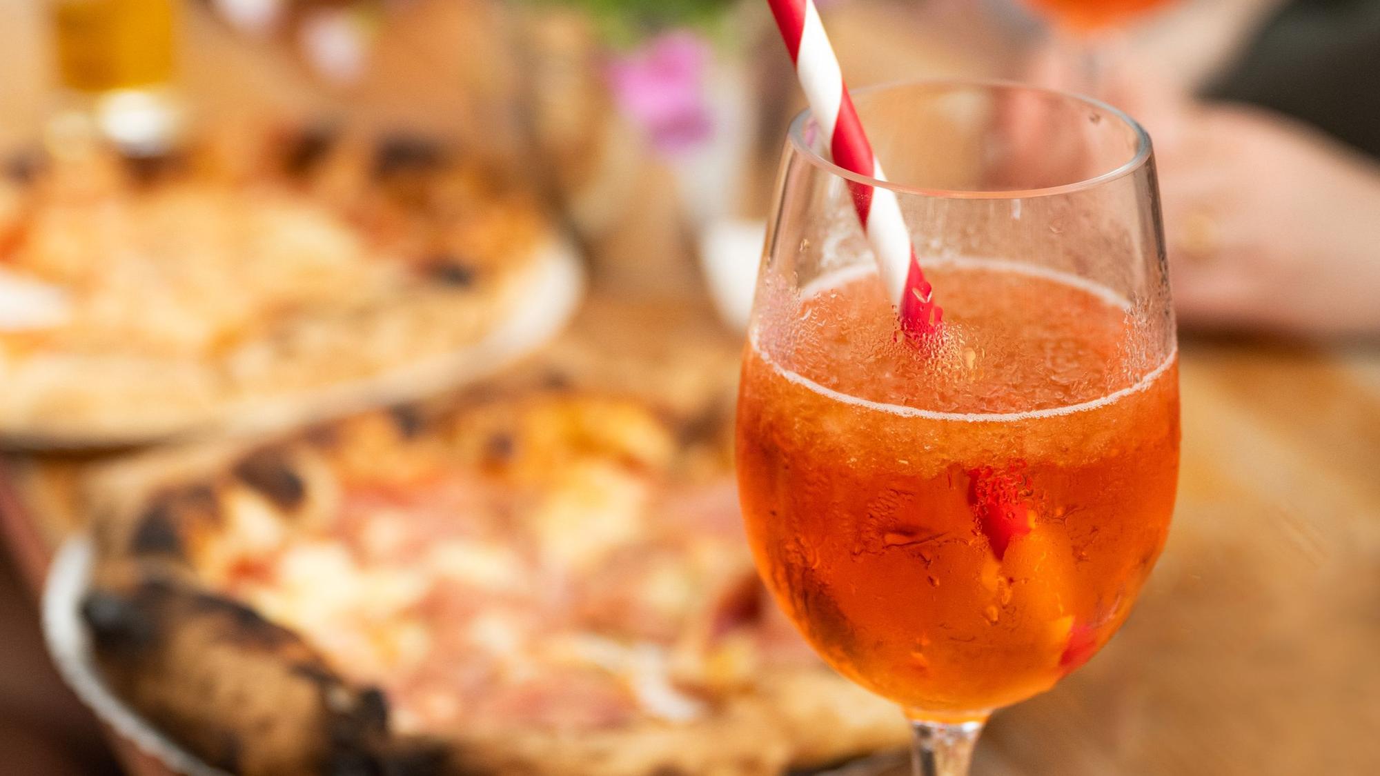 Aperol Spritz und Pizza auf einem Tisch bei einem Feierabendmarkt.