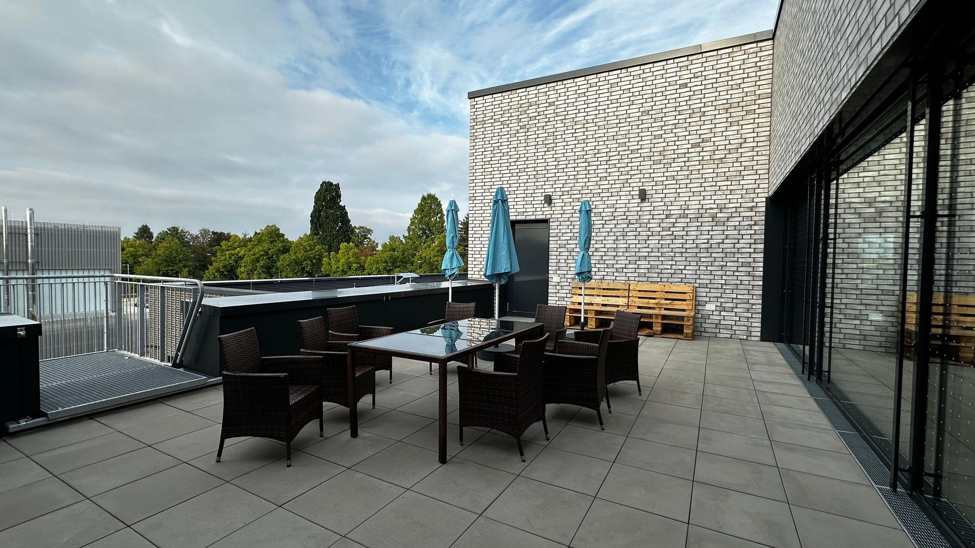 Auf einer Terrasse steht ein Tisch mit Stühlen und Sonnenschirmen.