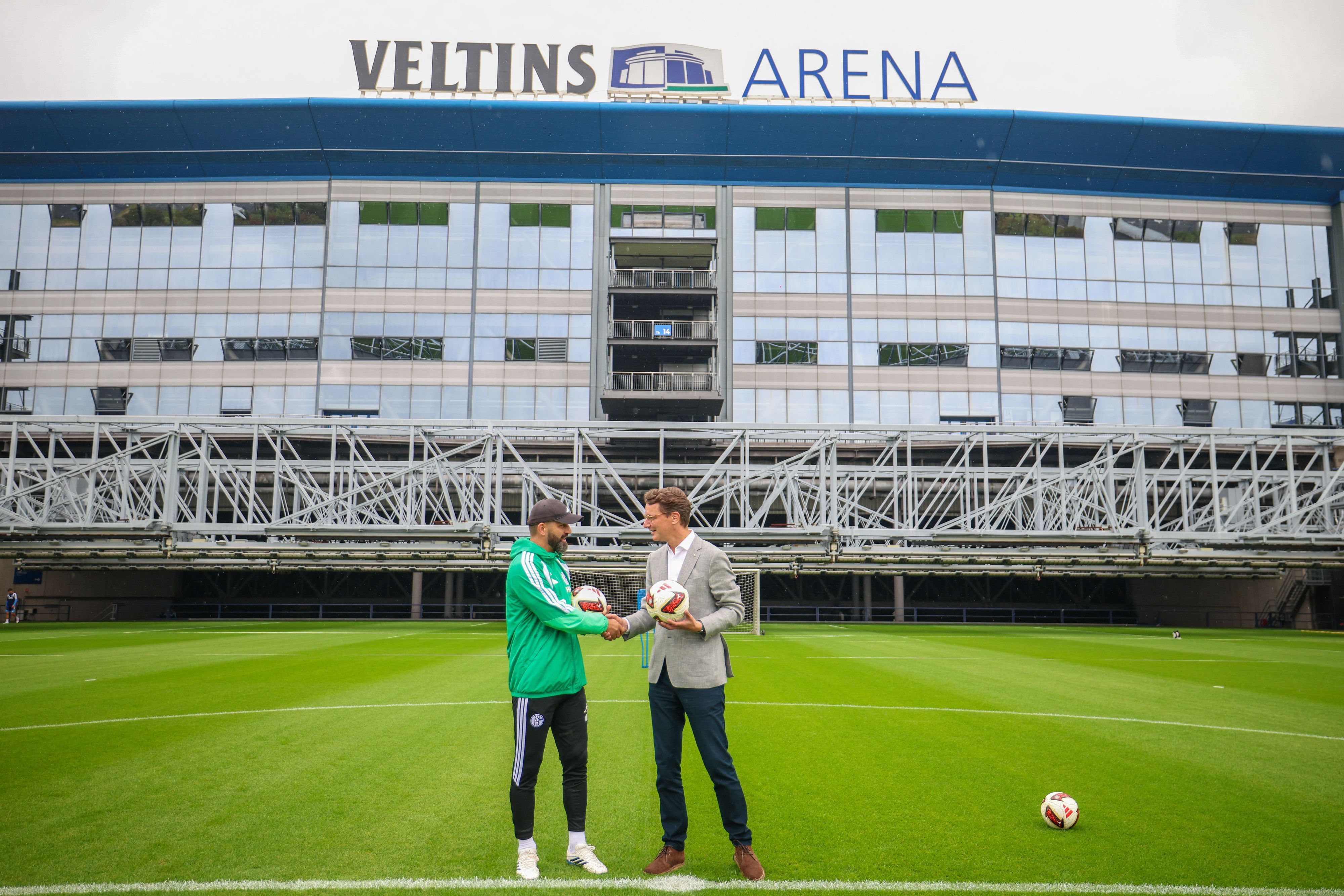 Miron Muslic, Trainer FC Schalke 04, und Hendrik Wüst (CDU), Ministerpräsident des Landes Nordrhein-Westfalen, stehen zusammen auf dem Rasen vor der Veltins-Arena.