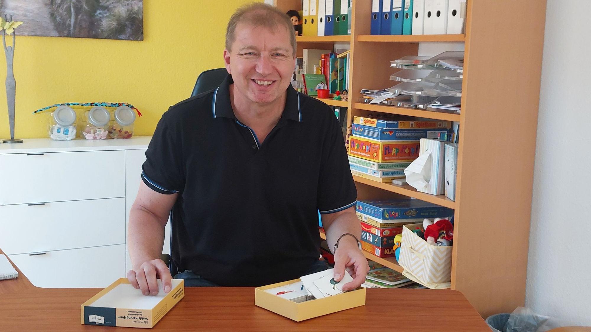 Auf dem Bild ist ein Mann zu sehen, der an einem Schreibtisch sitzt.