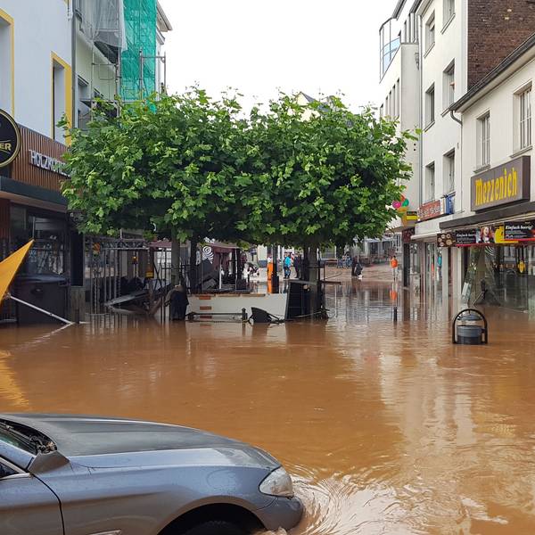 Das Wasser ist trüb-braun, ein Auto ist halb versunken, im Hintergund umgekipptes Gastronomie-Mobiliar.