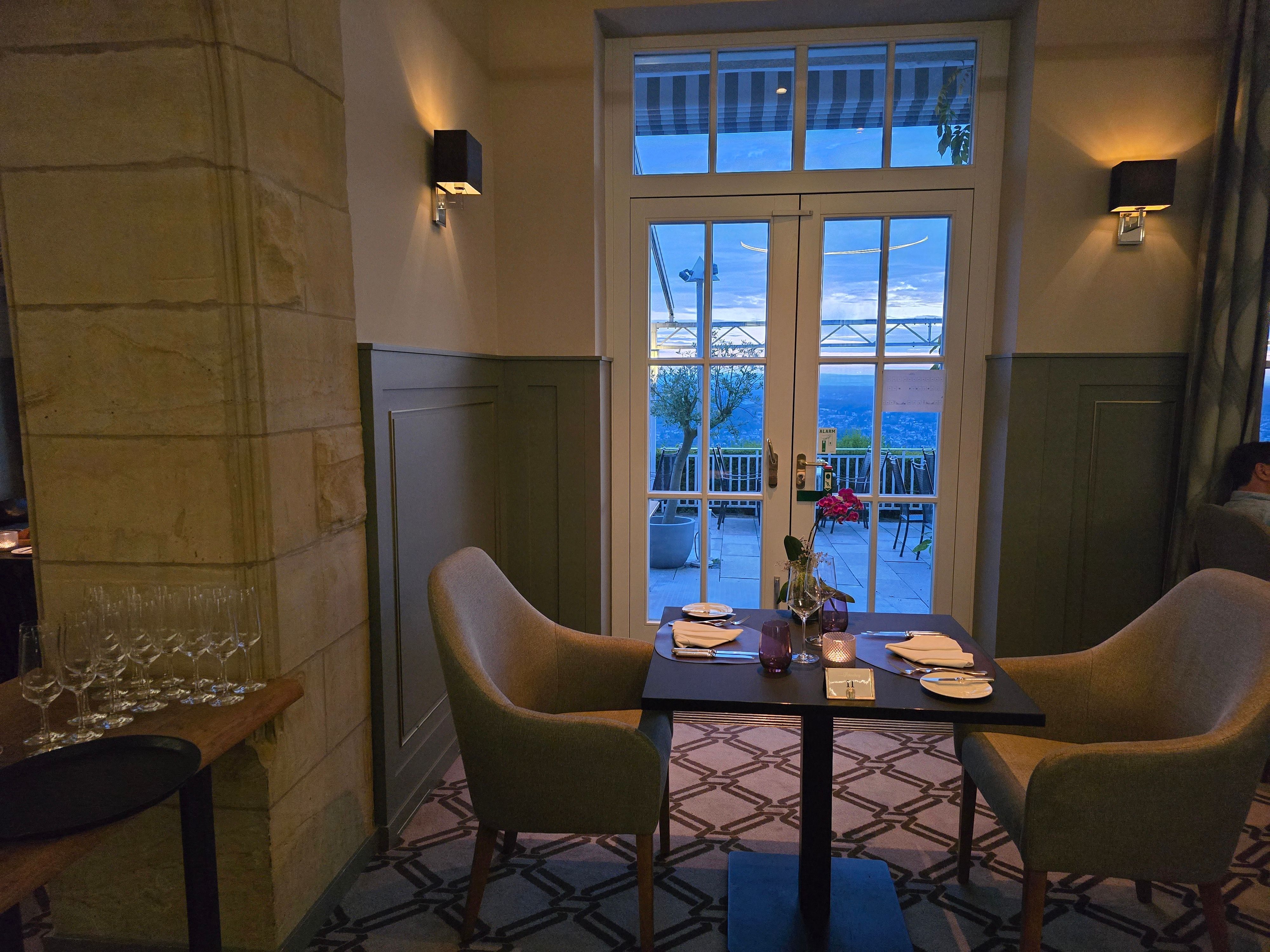 Das restaurant von innen: ein eingedeckter Tisch mit zwei Stühlen vor einem Fenster, das den Blick auf das Rheintal preisgibt.