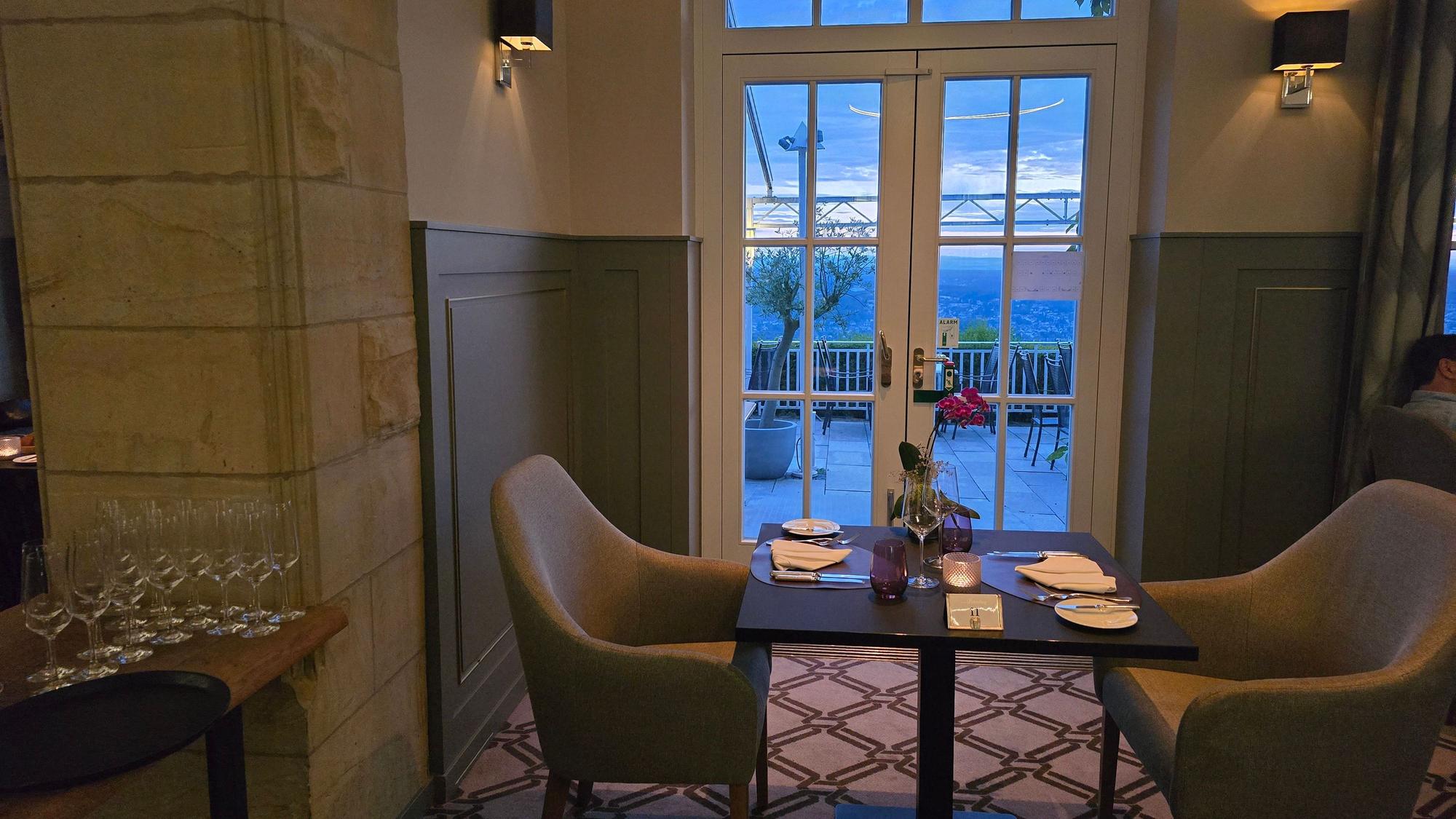 Das restaurant von innen: ein eingedeckter Tisch mit zwei Stühlen vor einem Fenster, das den Blick auf das Rheintal preisgibt.