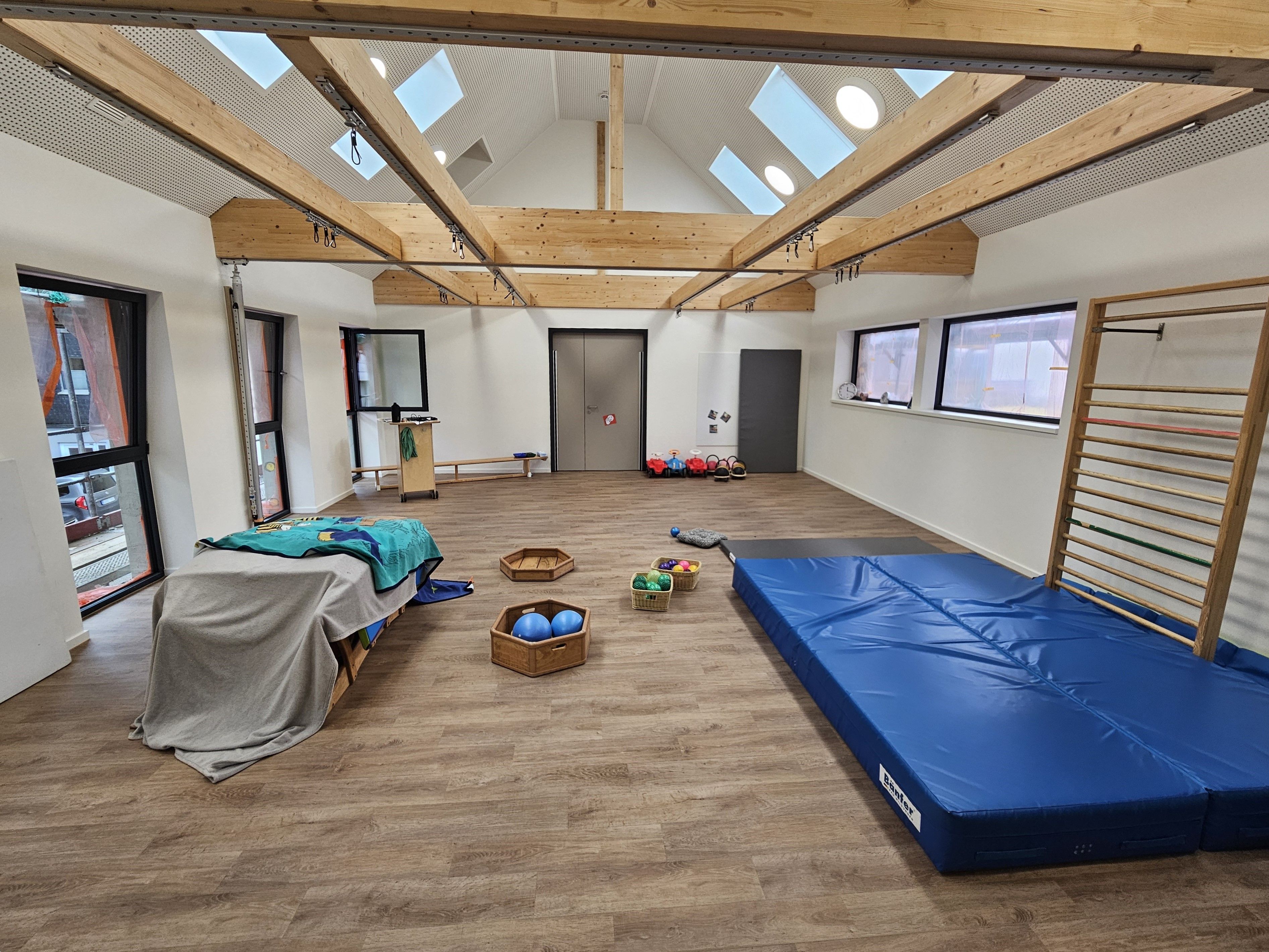 Blick in die kleine Turnhalle mit einer großen blauen Matte, Klettergerüst und Bällen.