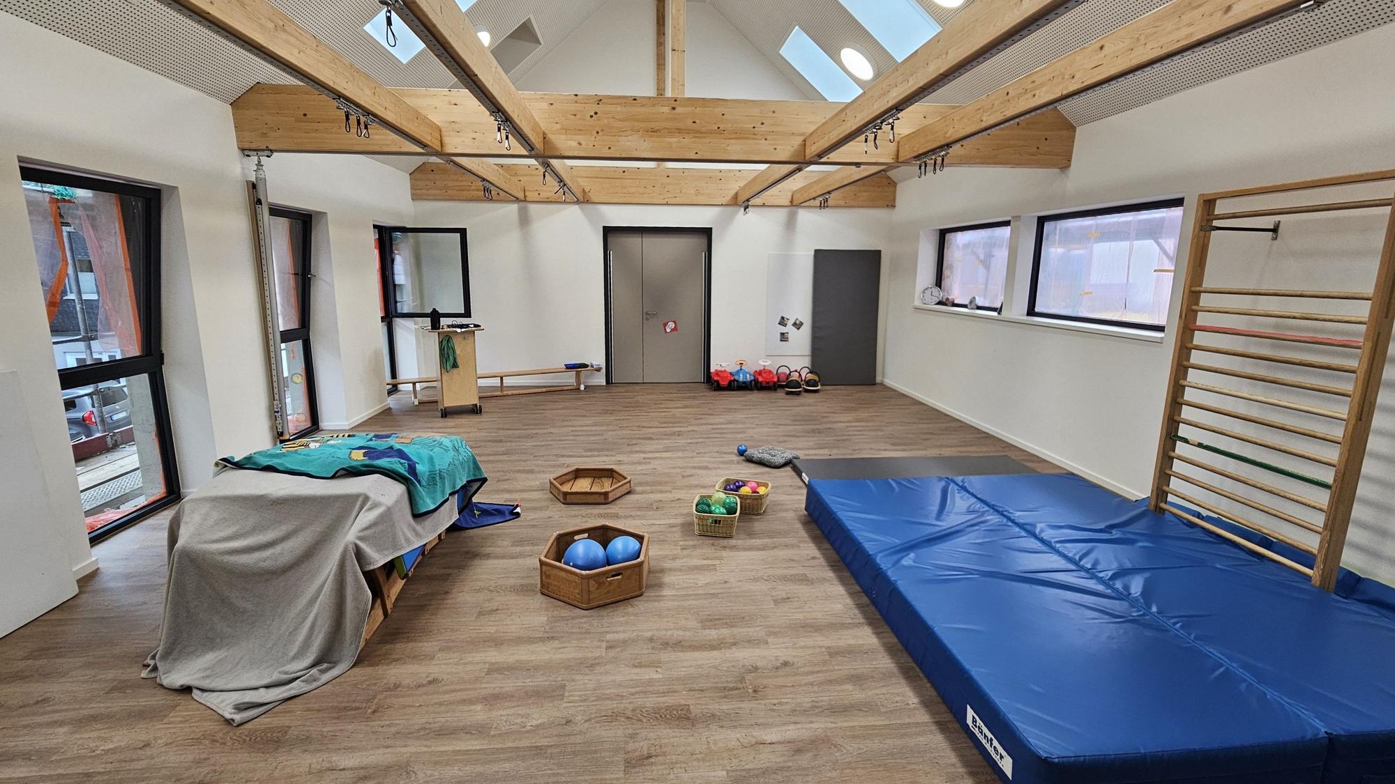 Blick in die kleine Turnhalle mit einer großen blauen Matte, Klettergerüst und Bällen.