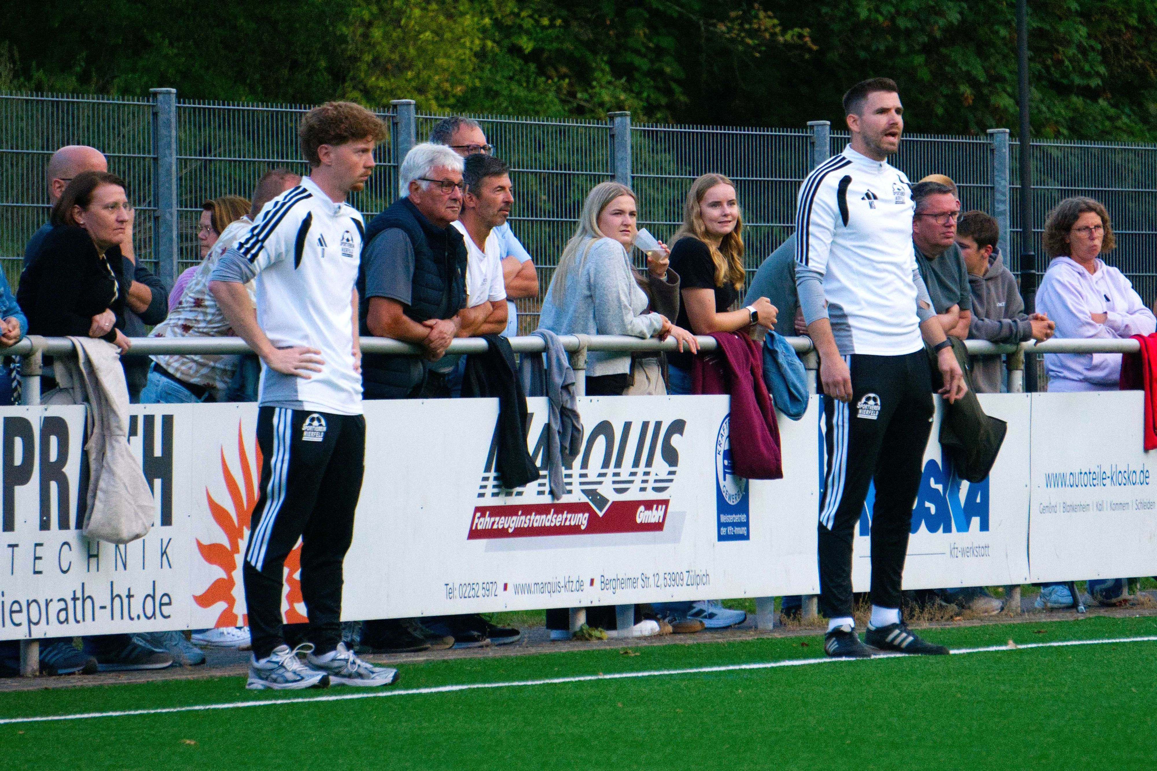 Die Beiden Trainer des SV Nierfeld stehen am Spielfeldrand und schauen auf den Fußballplatz.