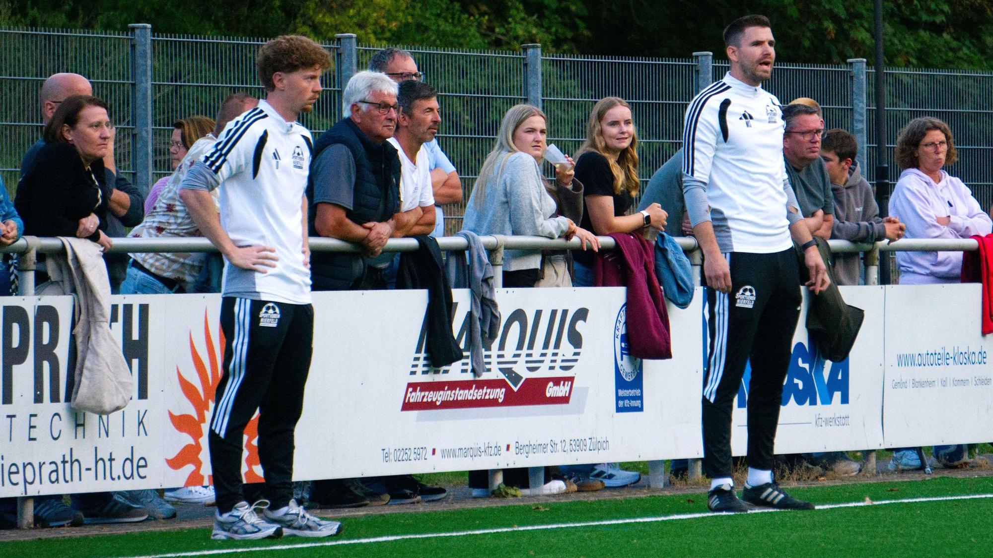 Die Beiden Trainer des SV Nierfeld stehen am Spielfeldrand und schauen auf den Fußballplatz.