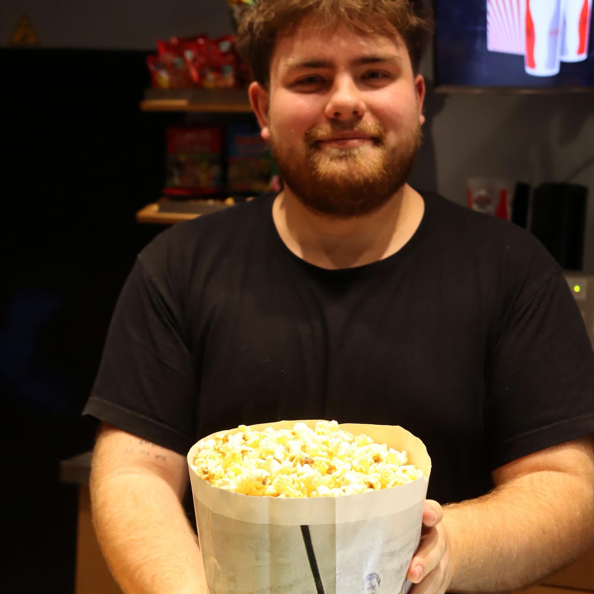 Ein Kinomitarbeiter hält eine Tüte Popcorn in den Händen.
