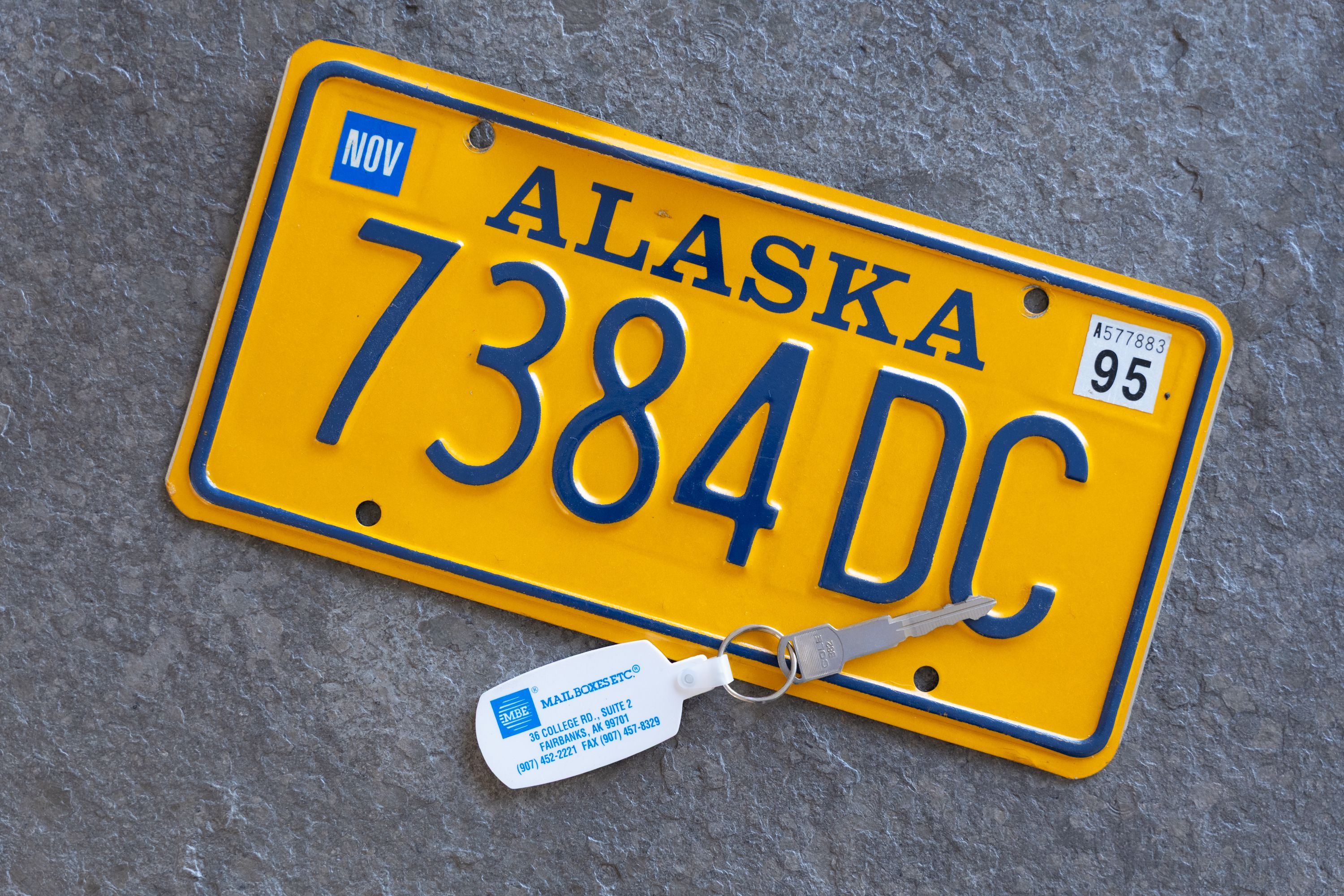 Ein gelbes Nummernschild und ein Autoschlüssel eines Mietwagens aus Alaska.