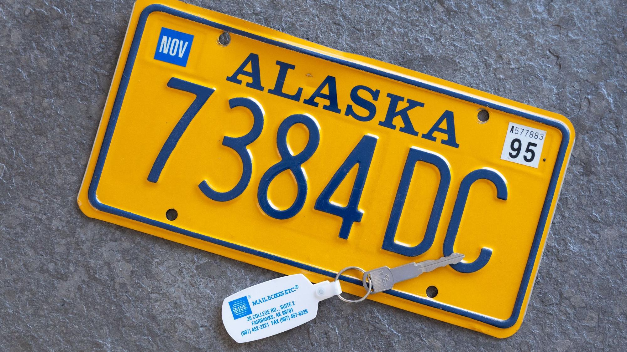 Ein gelbes Nummernschild und ein Autoschlüssel eines Mietwagens aus Alaska.
