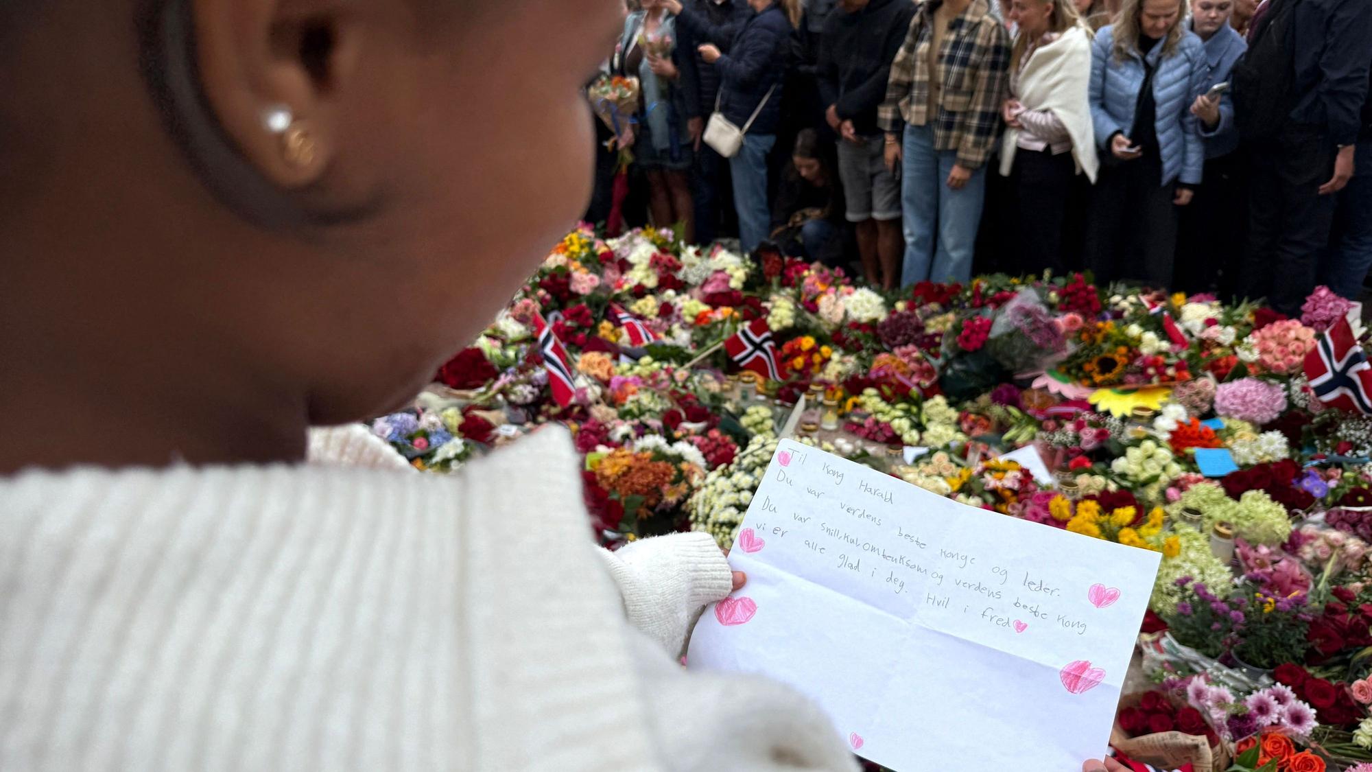 Die elfjährige Mina hält ihren selbstgeschriebenen Brief mit der Aufschrift „Du warst nett, cool, fürsorglich und der beste König der Welt“ zwischen den vor dem Königlichen Schloss Oslo abgelegten Blumen in den Händen.