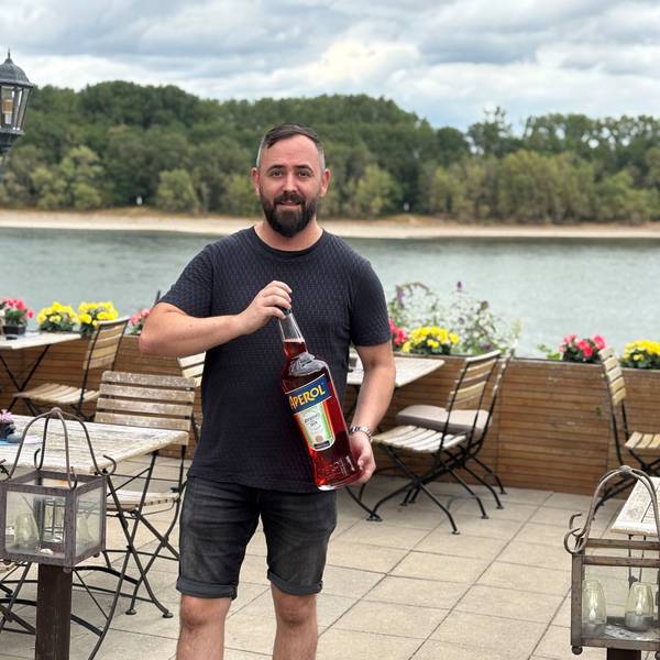 Auf dem Bild ist ein Mann zu sehen, der eine große Flasche Aperol in den Händen hält.