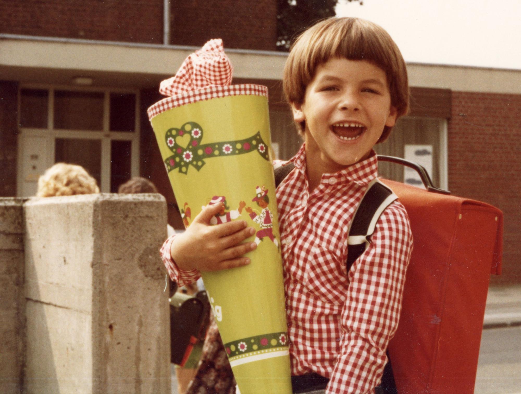 Ein Junge strahlt, er hält eine riesige Schultüte in der Hand.