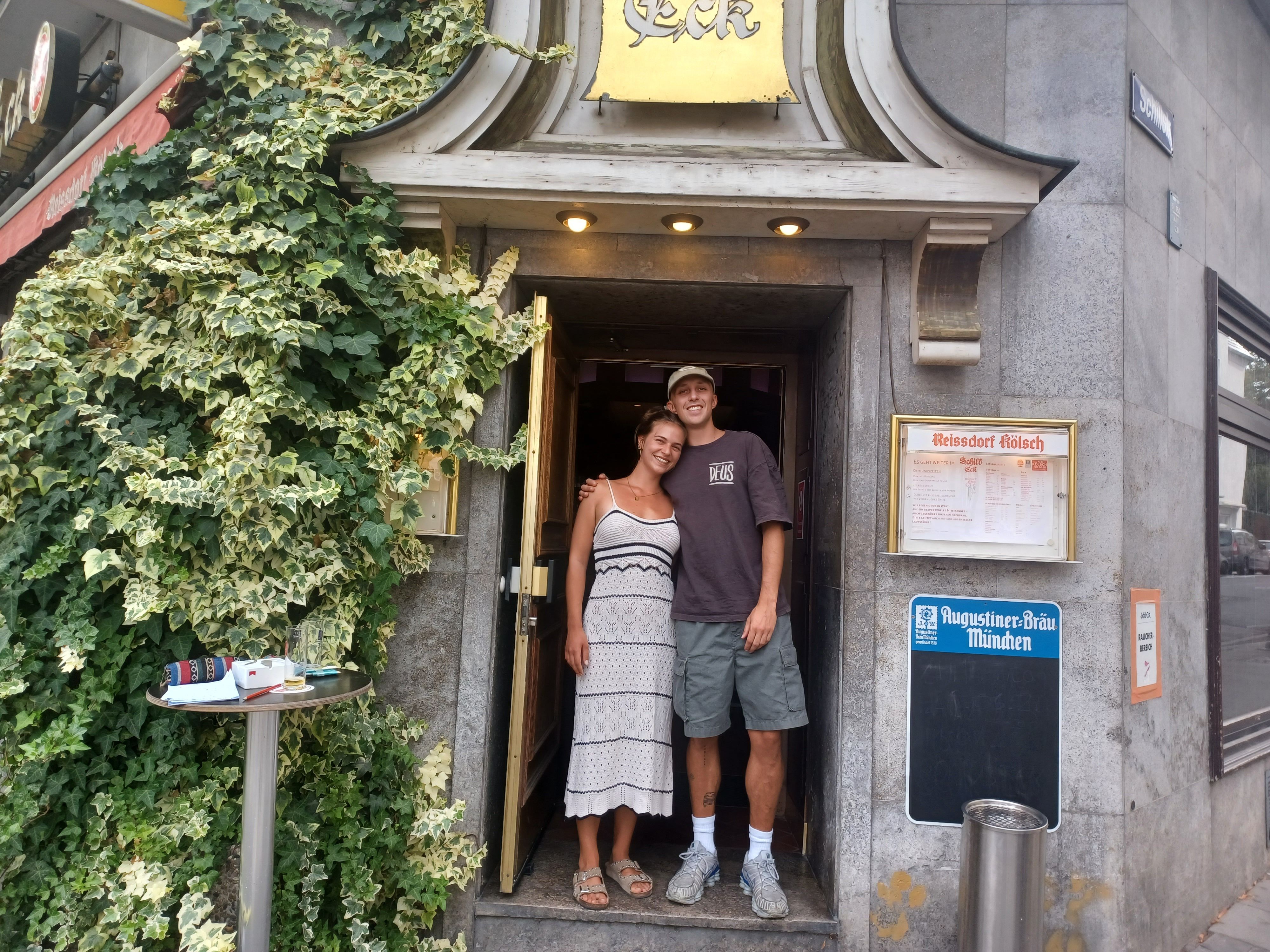 Eine junge Frau und ein junger Mann stehen in einem Kneipeneingang. Sie sind zwei der vier jungen Inhaber/-innen, die die Kneipe „Schill-Eck“ in Nippes übernommen haben.