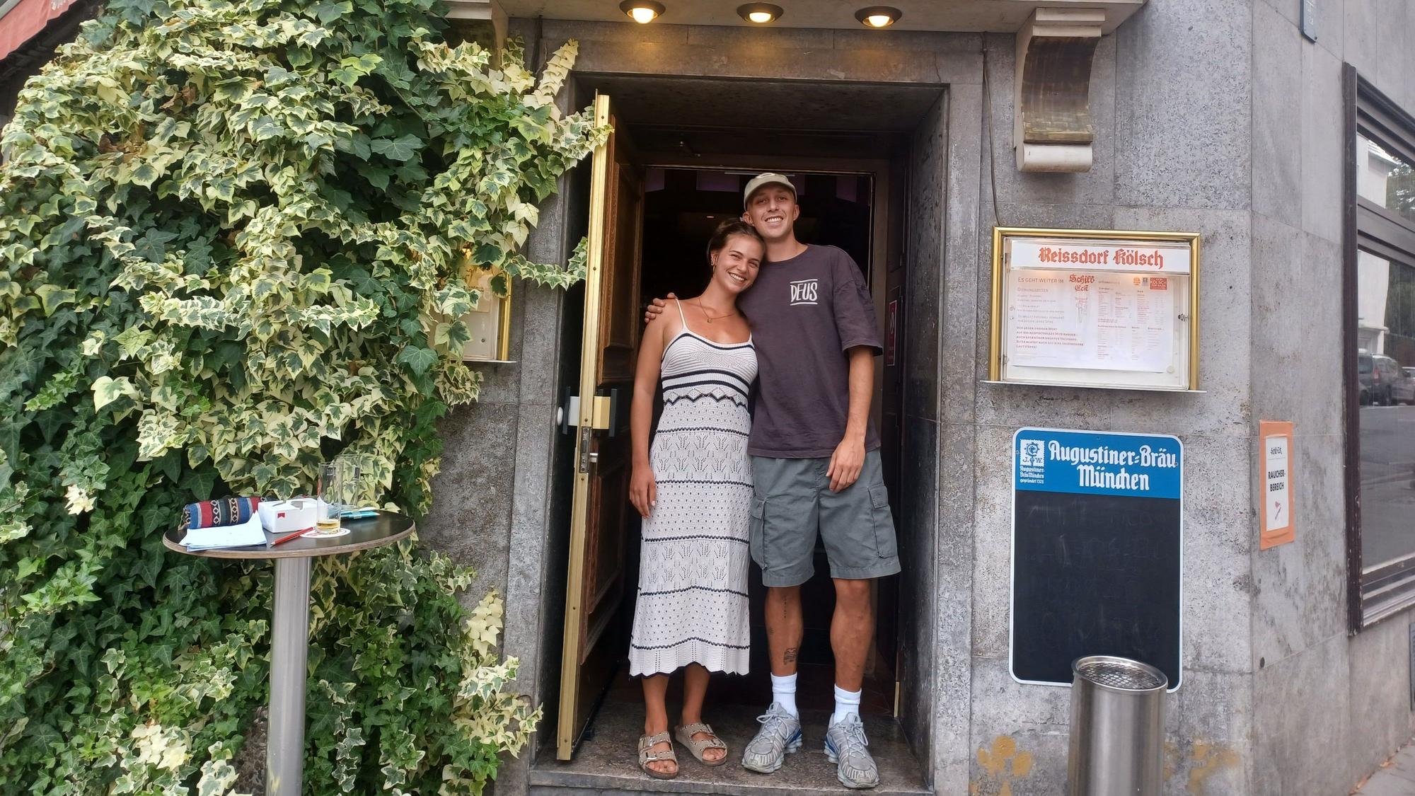 Eine junge Frau und ein junger Mann stehen in einem Kneipeneingang. Sie sind zwei der vier jungen Inhaber/-innen, die die Kneipe „Schill-Eck“ in Nippes übernommen haben.
