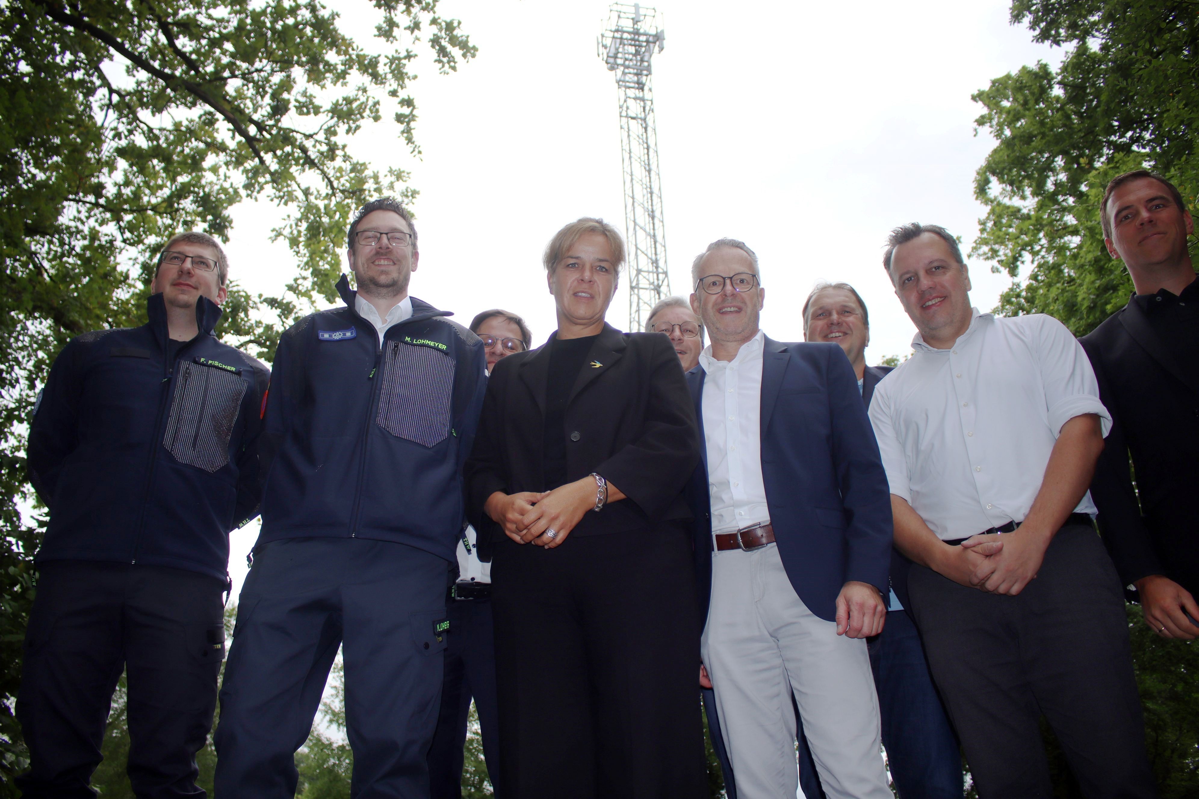 Eine Gruppe Menschen steht vor einem Mobilfunkmast an der Steinbachtalsperre bei Euskirchen.