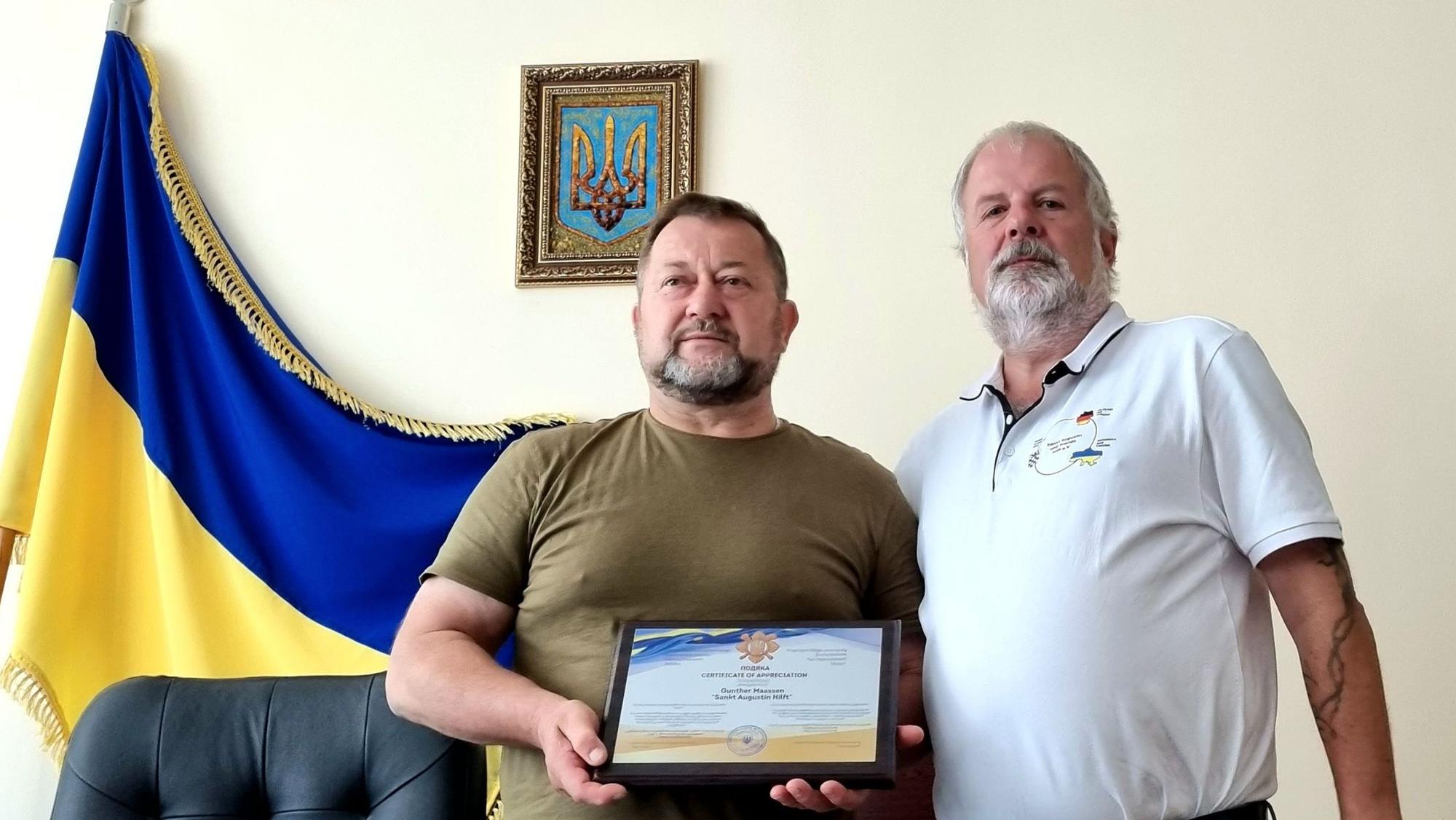 Zwei Männer neben einer ukrainischen Flagge.