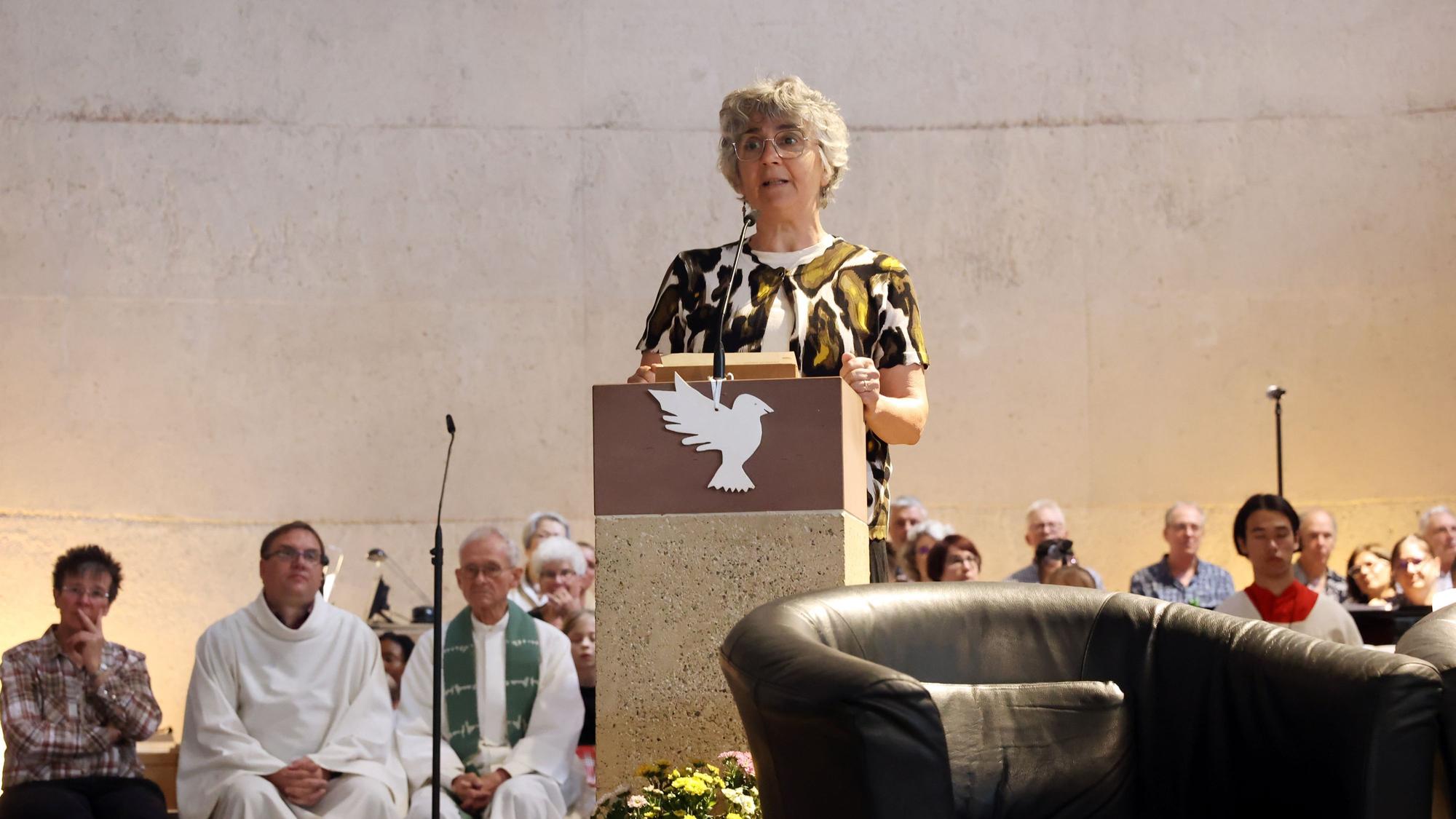 Eine Frau steht am Ambo in einer Kirche. Hinter ihr sind der Chor, der Pfarrer und Messdiener zu sehen.
