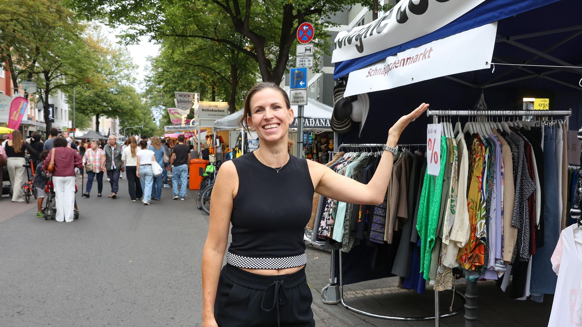 Eine Frau mit schwarzem Haar steht neben Kleiderständern an einem Straßenstand.