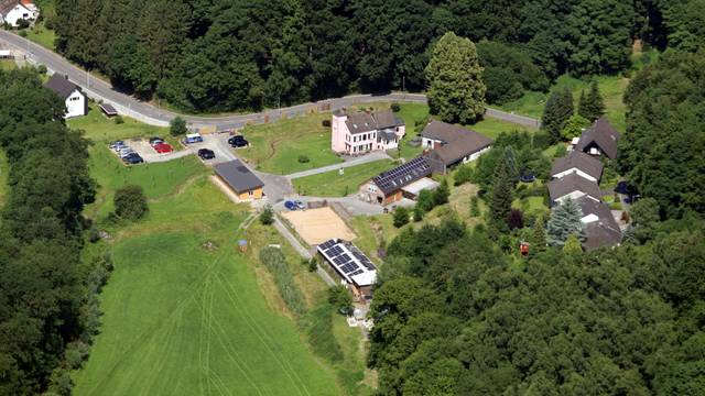 Eine Luftaufnahme mit viel Wiese und Bäumen, einer Straße und wenigen Gebäuden