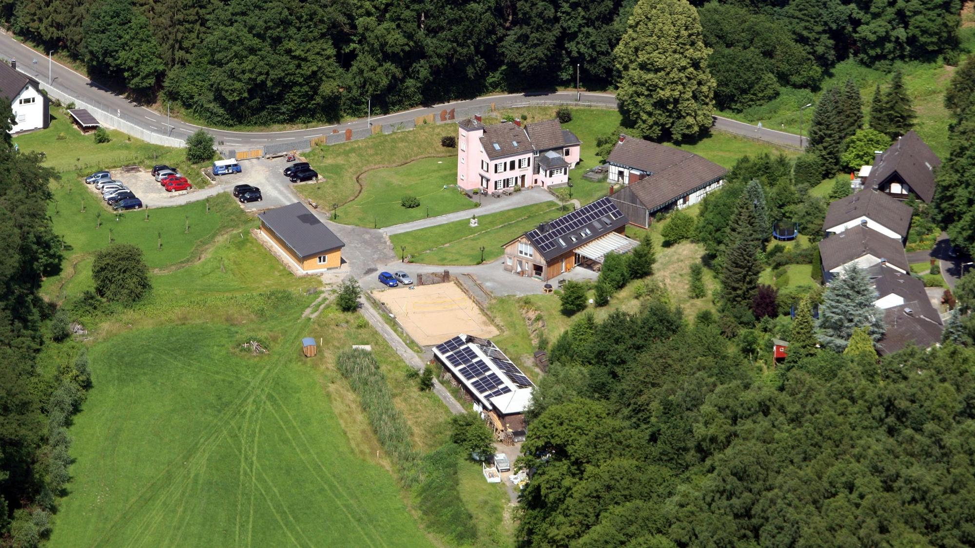 Eine Luftaufnahme mit viel Wiese und Bäumen, einer Straße und wenigen Gebäuden