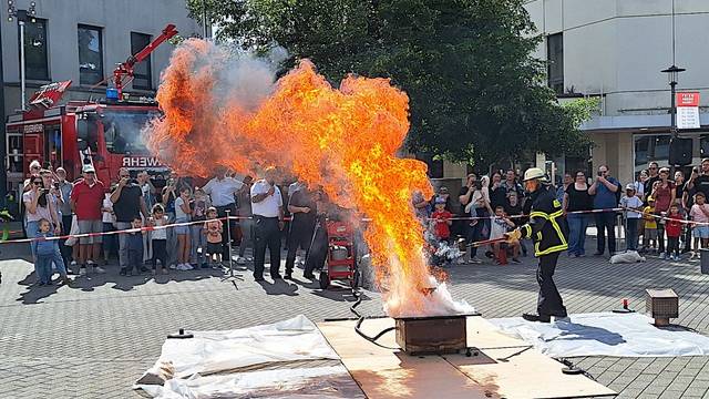 Ein Feuerwehrmann löscht eine hohe Stichflamme, Menschen hinter einer Absperrung schauen zu.