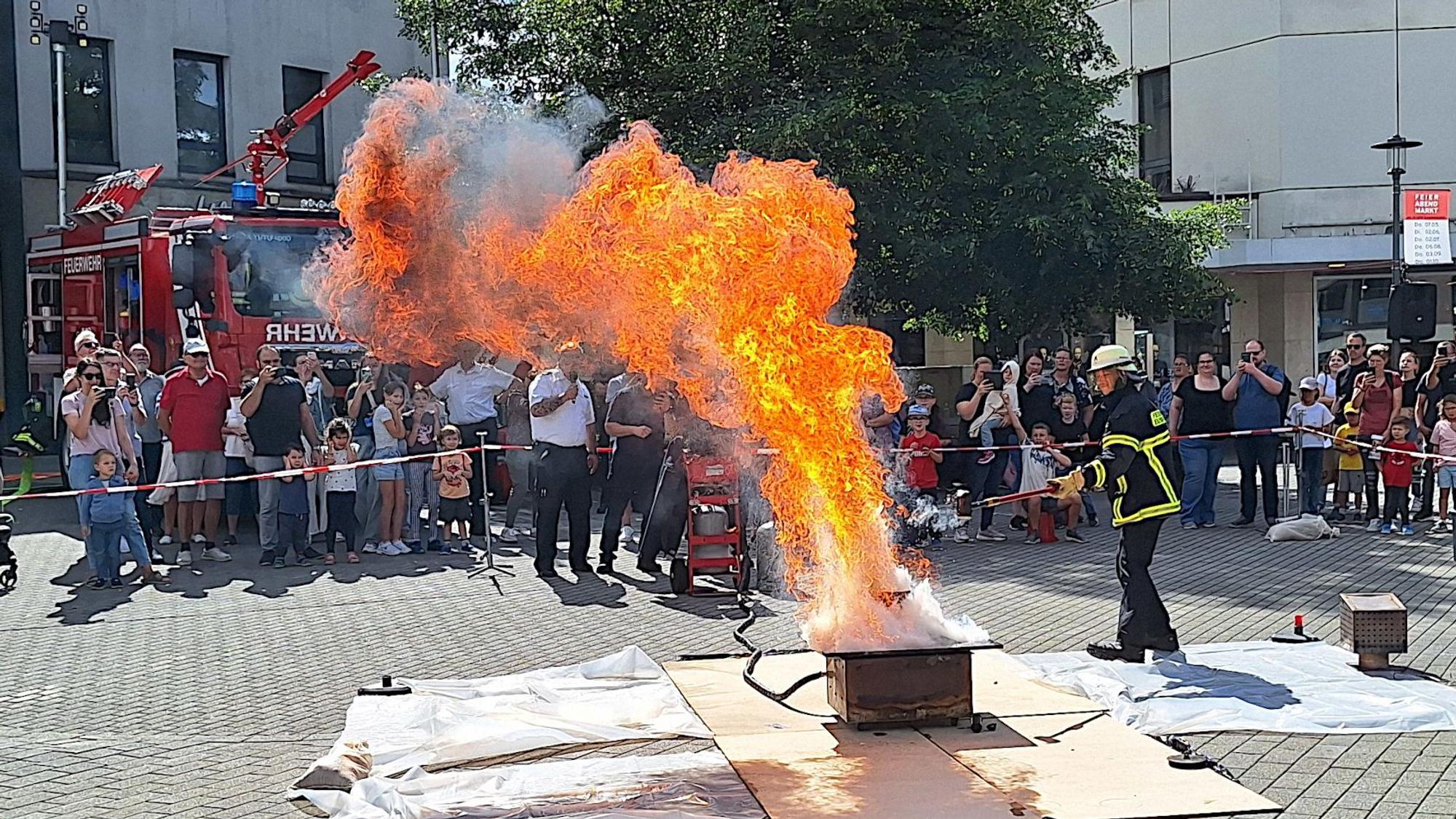 Ein Feuerwehrmann löscht eine hohe Stichflamme, Menschen hinter einer Absperrung schauen zu.