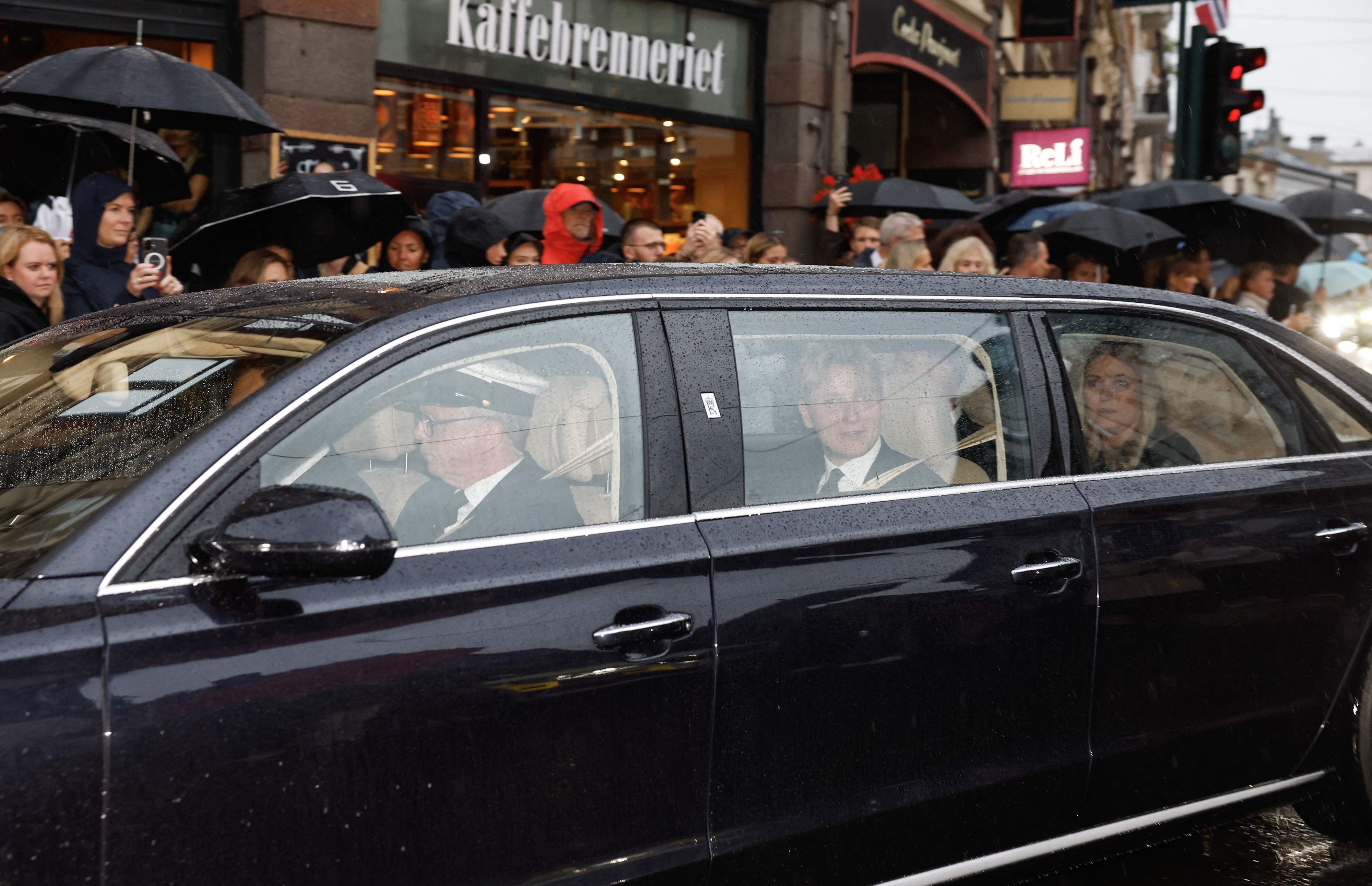 Norwegens neue Königin Mette-Marit (r.) und Norwegens Prinz Sverre Magnus (M.) sitzen in einem Auto hinter dem Leichenwagen mit dem verstorbenen König Harald V. von Norwegen, während dieser am 28. August 2026 durch Oslo in Richtung des Königlichen Schlosses fährt.