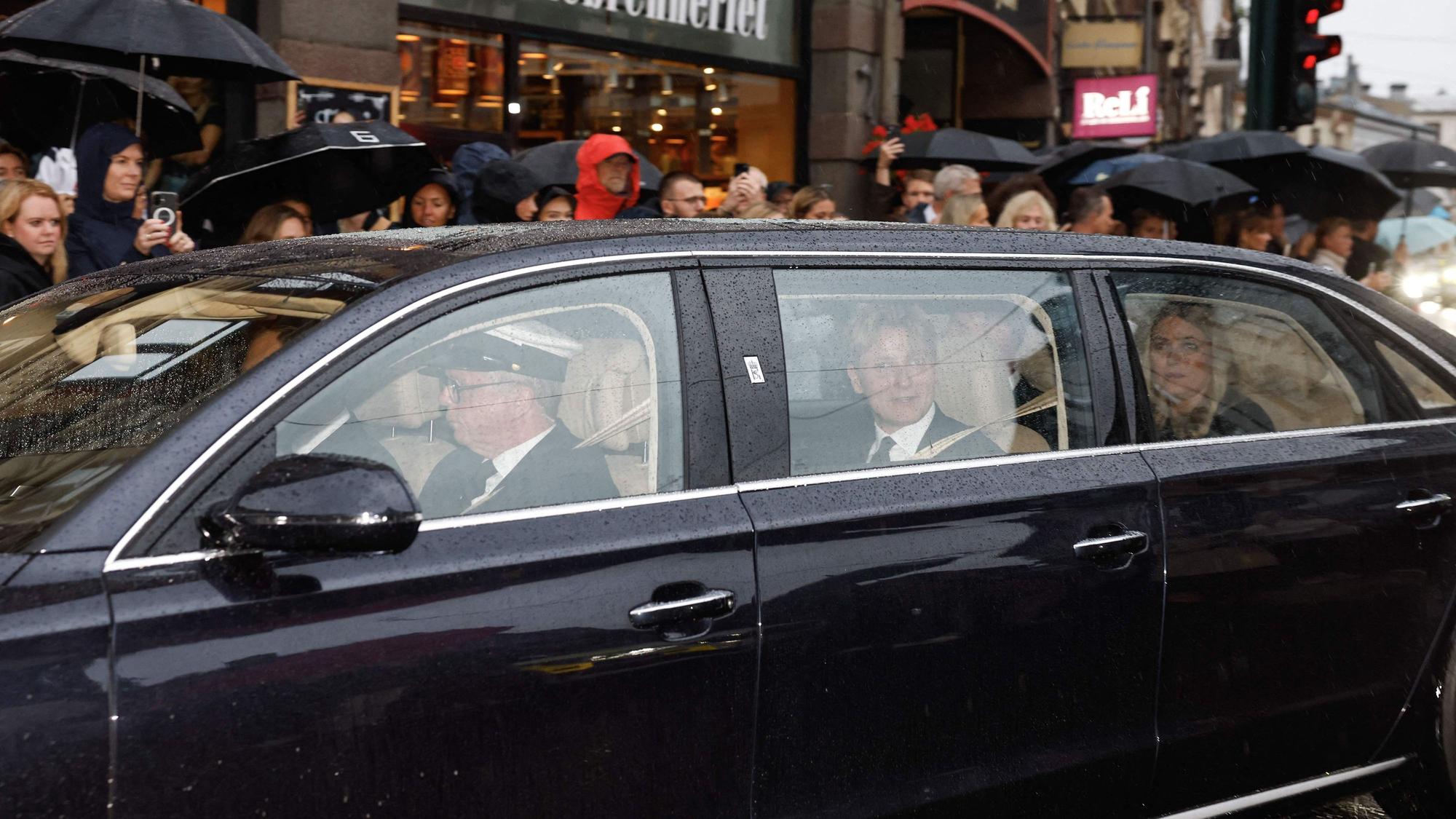 Norwegens neue Königin Mette-Marit (r.) und Norwegens Prinz Sverre Magnus (M.) sitzen in einem Auto hinter dem Leichenwagen mit dem verstorbenen König Harald V. von Norwegen, während dieser am 28. August 2026 durch Oslo in Richtung des Königlichen Schlosses fährt.