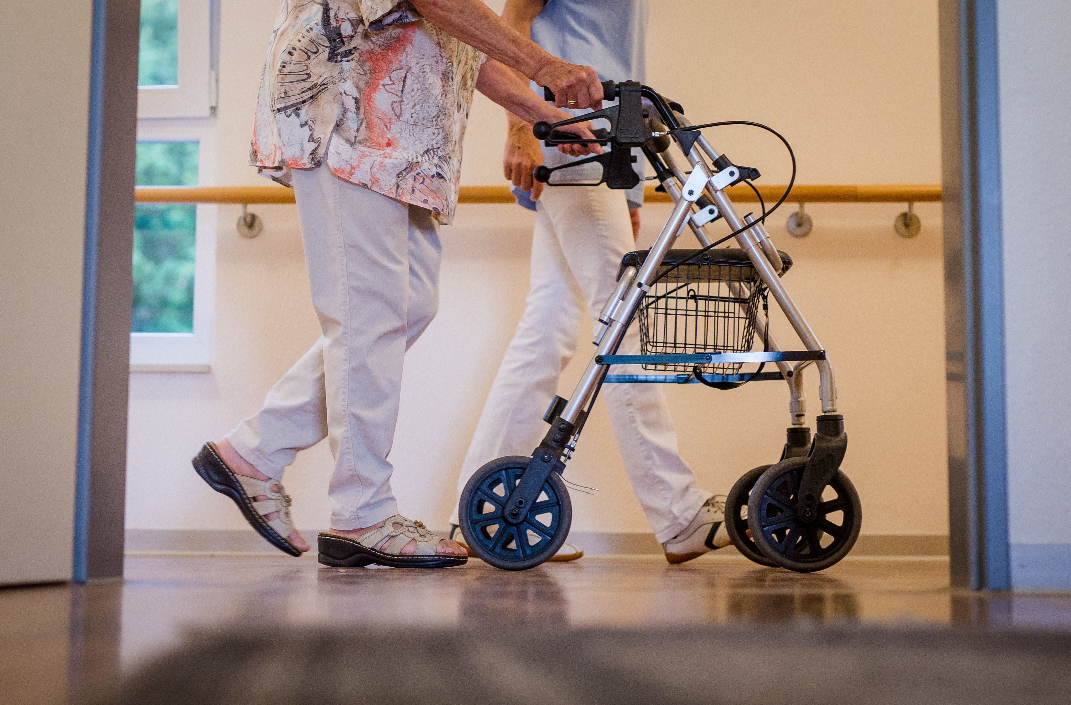 Eine Pflegekraft geht in einem Pflegeheim mit einer älteren Dame über einen Korridor.