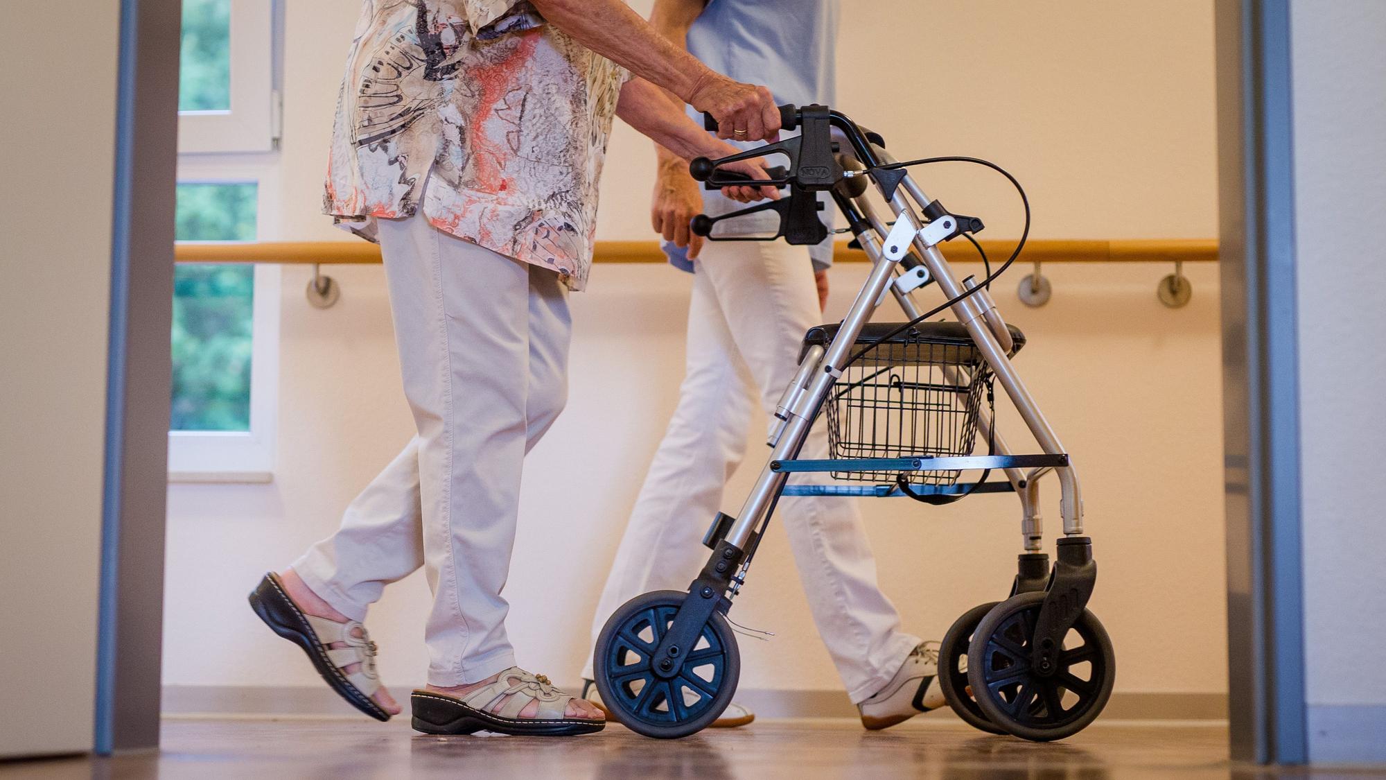 Eine Pflegekraft geht in einem Pflegeheim mit einer älteren Dame über einen Korridor.