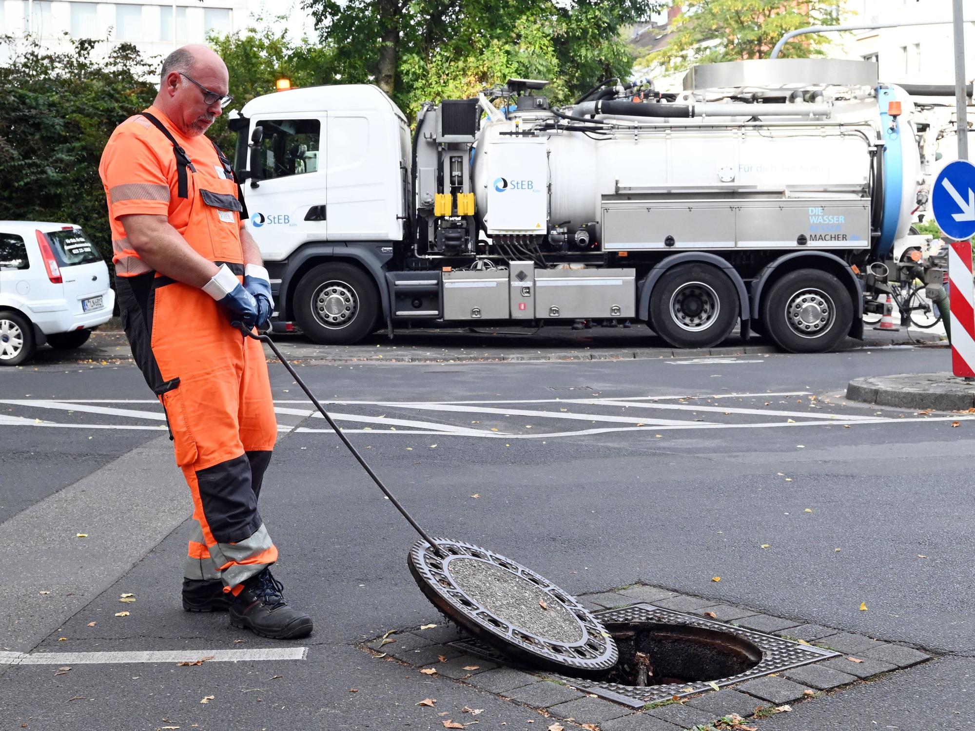 Ein Mann im orangefarbenen Anzug öffnet einen Kanaldeckel