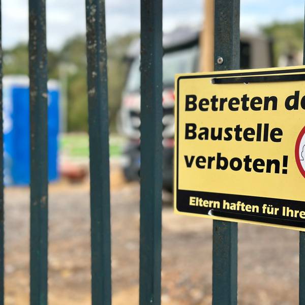 Ein gelbes Schild mit der Aufschrift „Betreten der Baustelle verboten“ hängt an einem Zaun.