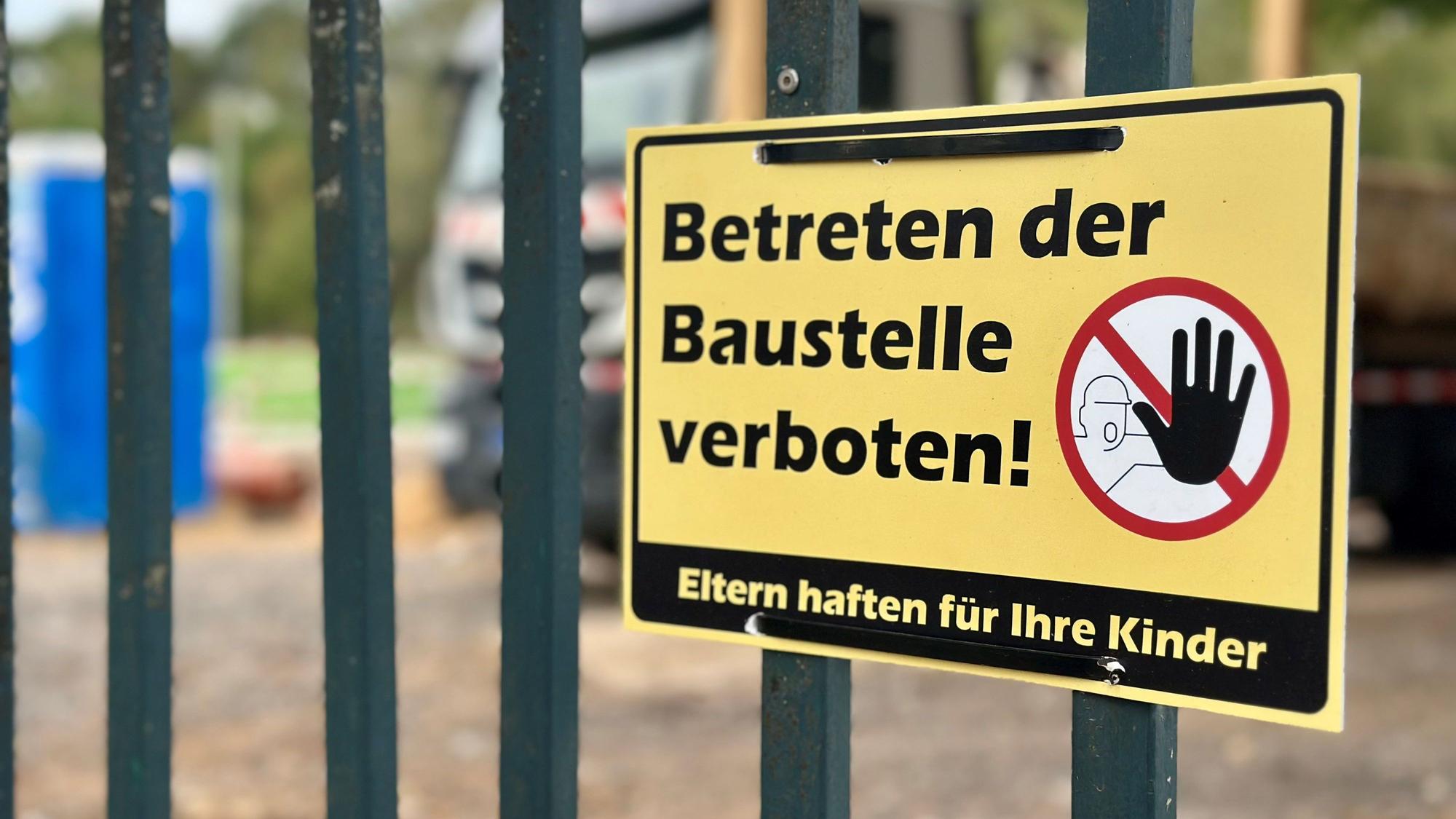 Ein gelbes Schild mit der Aufschrift „Betreten der Baustelle verboten“ hängt an einem Zaun.
