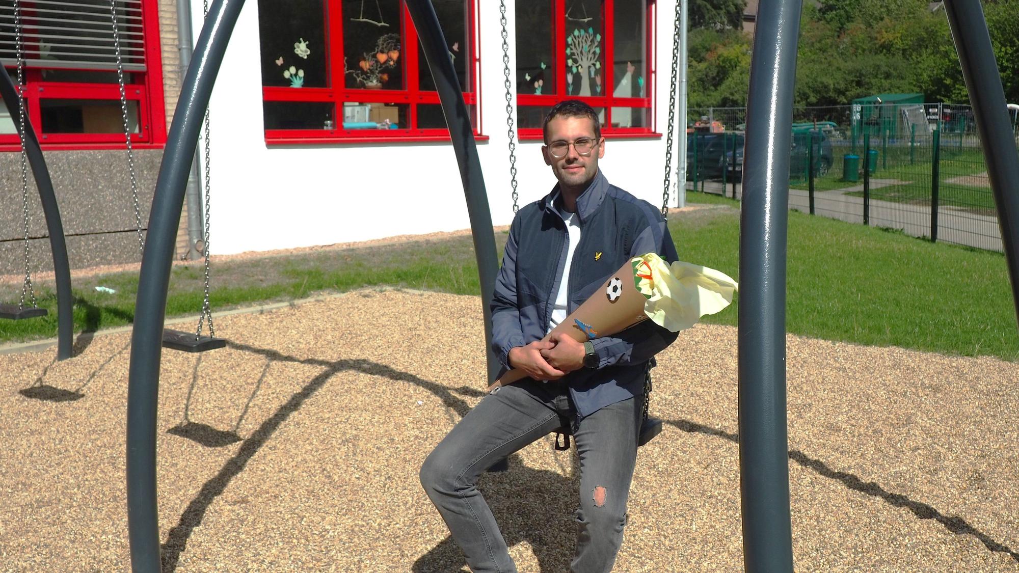 Mechernichs neuer Schulleiter Martin Schmitz hält eine Schultüte in der Hand und sitzt auf einer Schaukel.