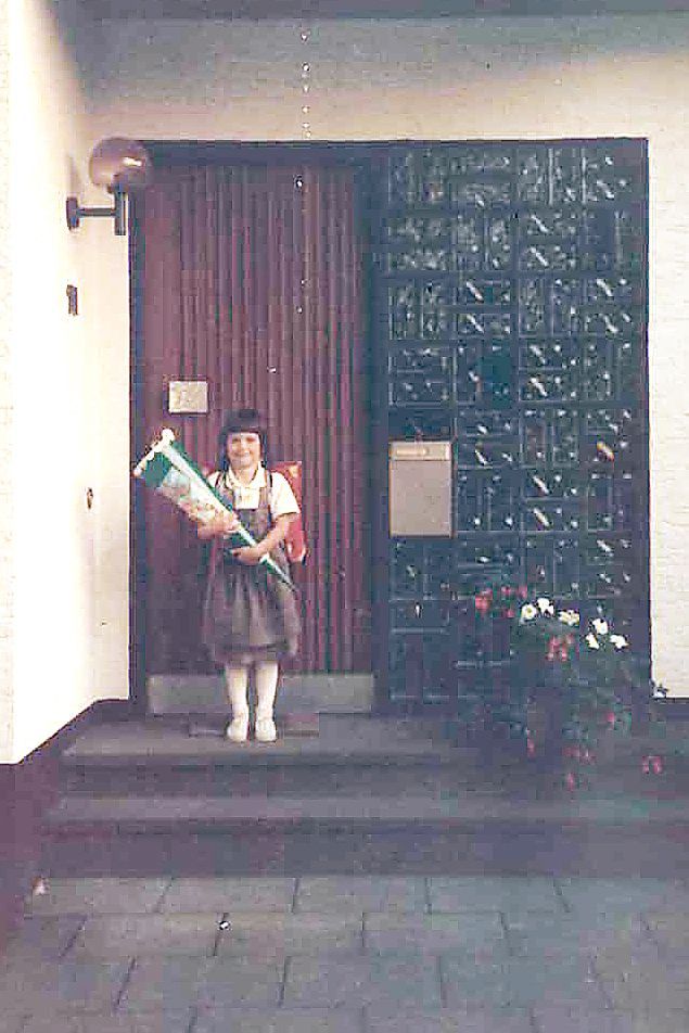 Ein Mädchen mit Schultüte und Ranzen steht vor einem Haus.