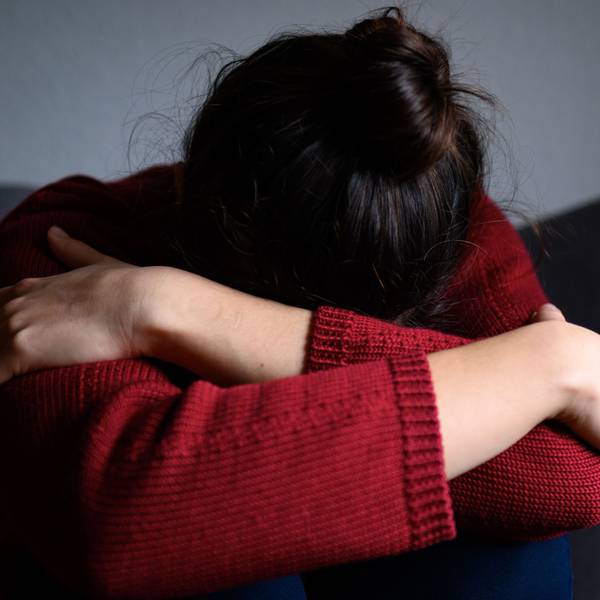 Eine Frau sitzt mit dem Kopf in den Armen versunken auf einem Stuhl.