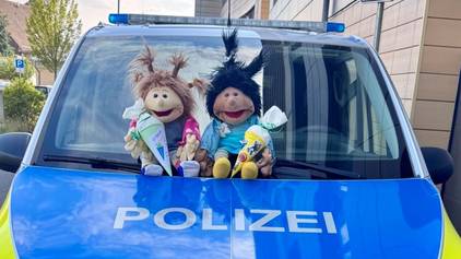 Zwei Stofffiguren sitzen vor der Windschutzscheibe eines Polizeiwagens.