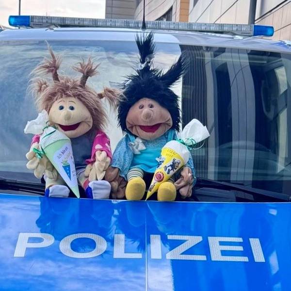 Zwei Stofffiguren sitzen vor der Windschutzscheibe eines Polizeiwagens.