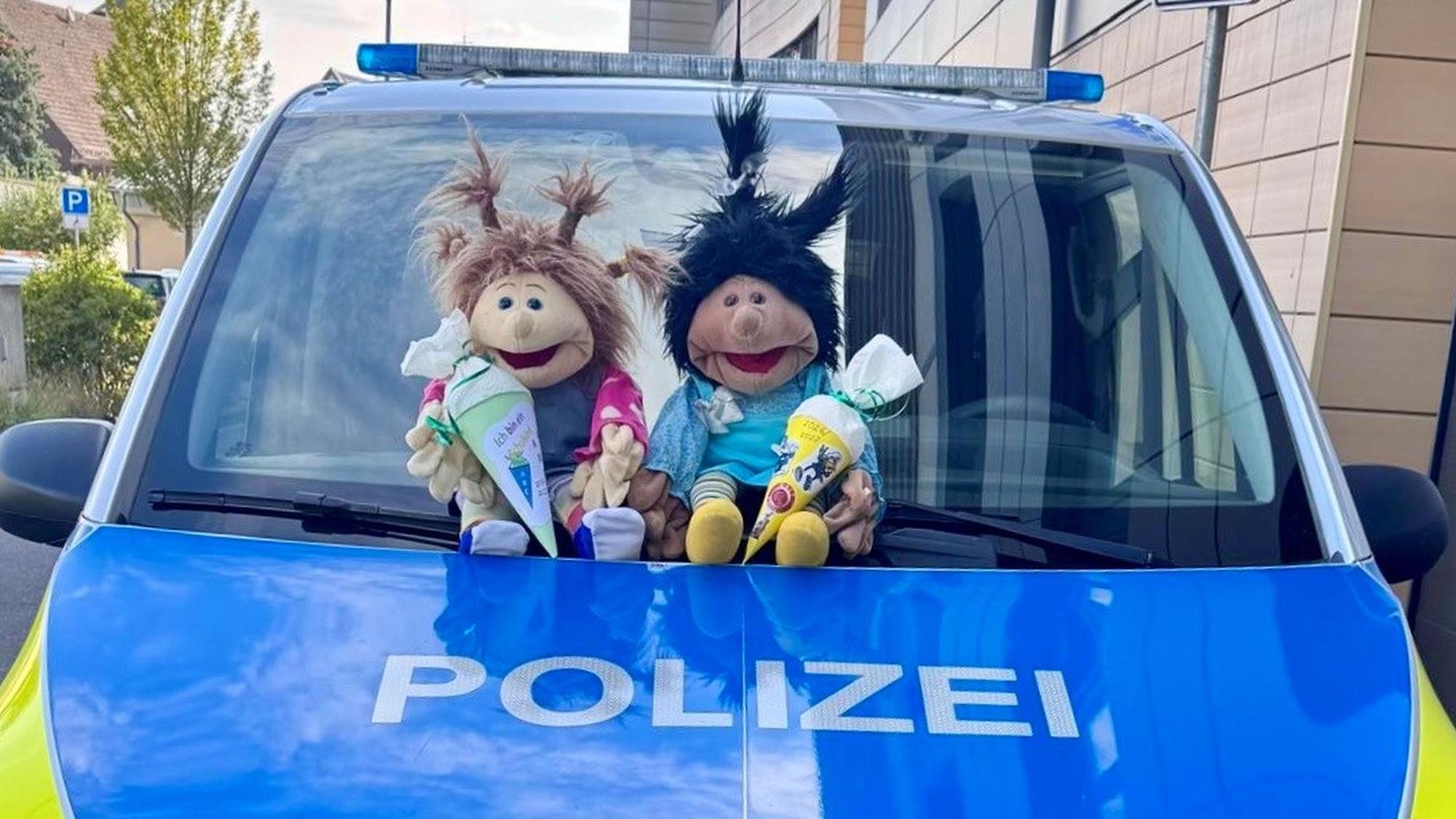 Zwei Stofffiguren sitzen vor der Windschutzscheibe eines Polizeiwagens.